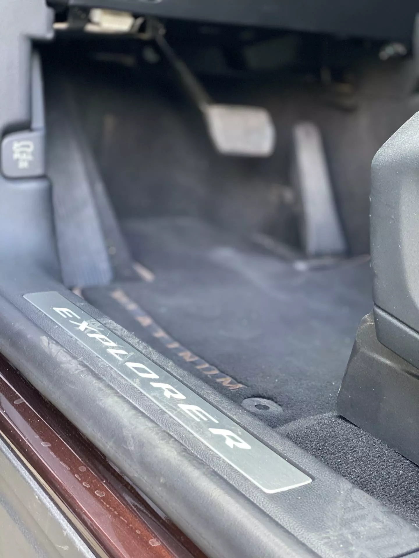 Zbliżenie wnętrza SUV-a Ford Explorer z 2019 roku, ukazujące szczegółowo obszar progu drzwiowego z płyta ze szczotkowanego metalu z wygrawerowanym logo 'Explorer'. Zdjęcie podkreśla próg, przez który wchodzą pasażerowie, z ciemnym dywanikiem, uszczelkami i miękkim naturalnym oświetleniem.