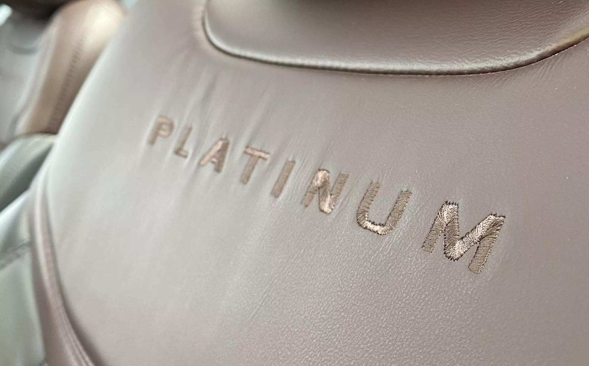 Zbliżenie na tapicerkę wnętrza Forda Explorera 2019, z wytłoczonym na gładkiej powierzchni 'PLATINUM', z lekkim kątem ukośnym. Tekst jest w centrum uwagi, z miękkim, równomiernie rozproszonym oświetleniem i płytką głębią ostrości.