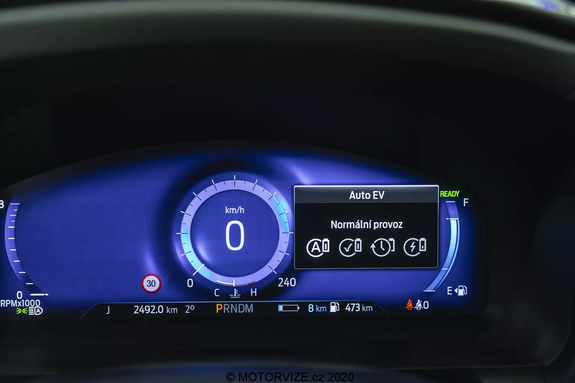 Zbliżenie cyfrowego zestawu wskaźników Forda Explorera 2019 z perspektywy kierowcy. Cyfrowy prędkościomierz pokazuje 0 km/h, a panel instrumentów zawiera tryb 'Auto EV', wskazujący na elektryczny lub hybrydowy system napędu, status 'Gotowy', ikony dla funkcji automatycznego prowadzenia, licznik przebiegu na 24 920 km, wskaźnik biegu PRNDM, ikony stanu dla baterii i oświetlenia zewnętrznego, wyświetlenie zużycia paliwa z 8 km pozostałego i maksymalnym zasięgiem 473 km, cyfrowy wskaźnik paliwa oraz brak świateł ostrzegawczych. Niebieski motyw kolorystyczny oferuje nowoczesną estetykę.