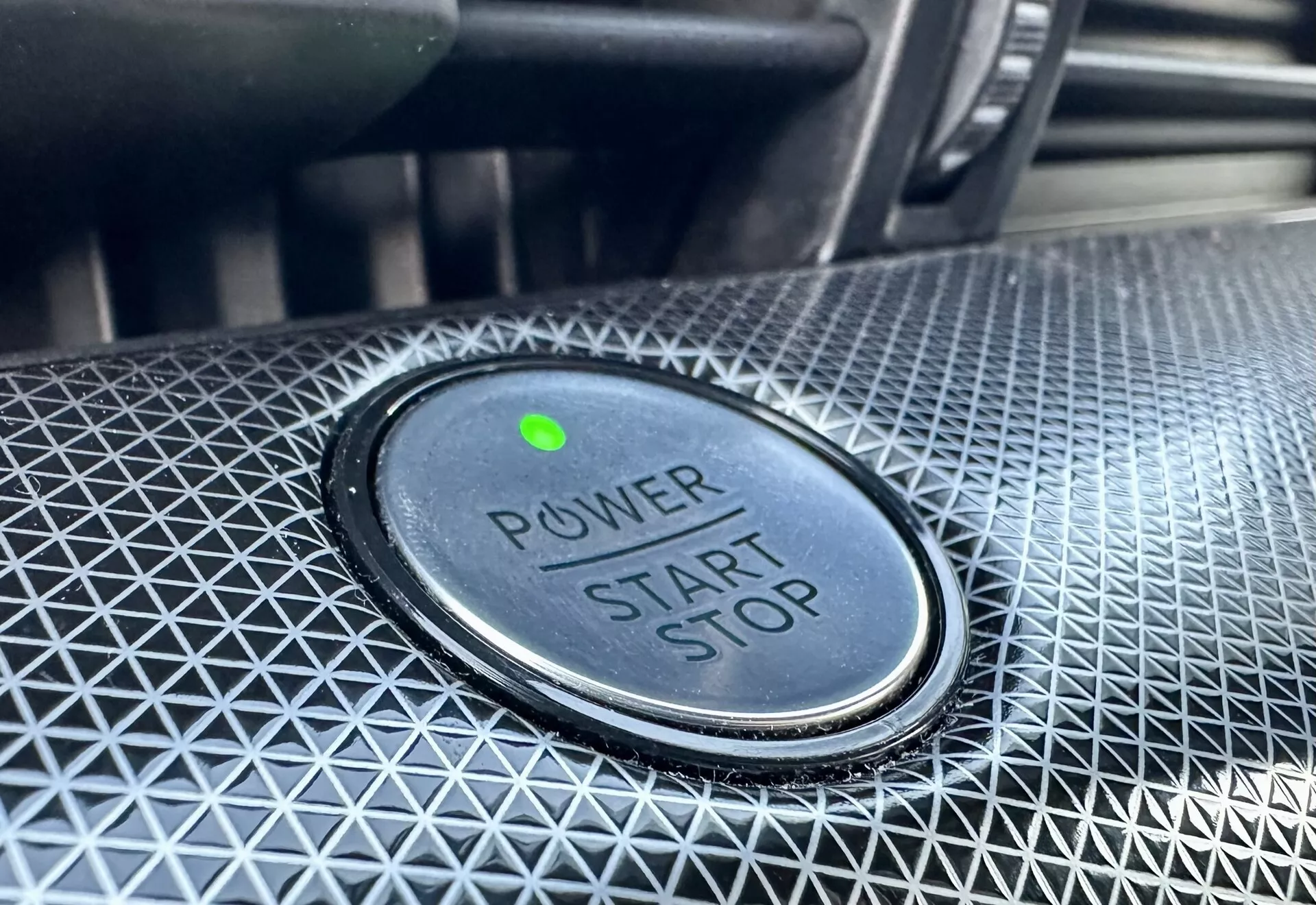Zbliżone zdjęcie przycisku start/stop mocy w Ford Mustang-Mach-E 2020 z napisem 'POWER START STOP', zieloną lampką kontrolną i teksturowanym wzornictwem wokół