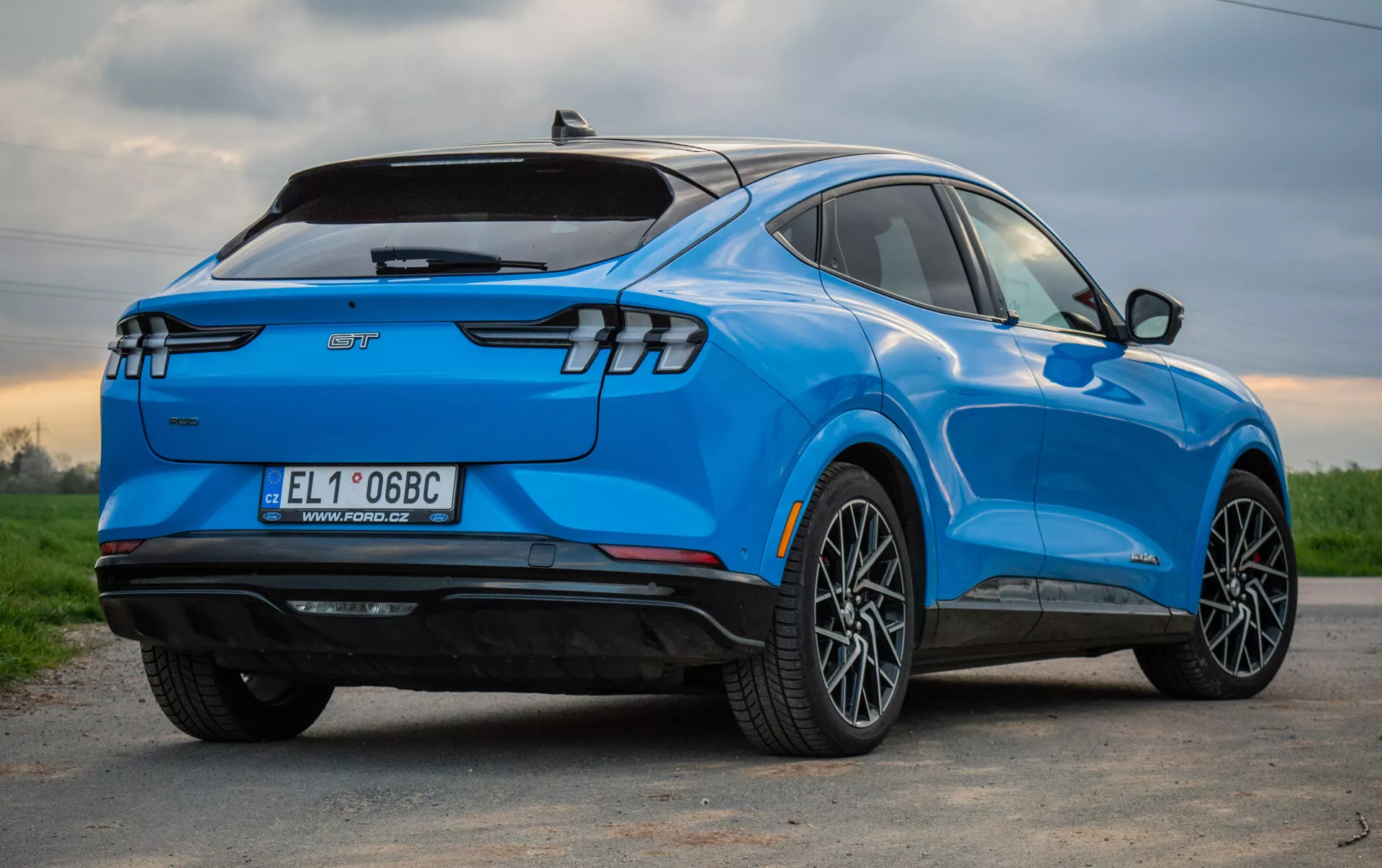 Niebieskie elektryczne SUV Ford Mustang Mach-E 2020 widziane z perspektywy trzy czwartej z tyłu, podkreślające jego stylowy aerodynamiczny design, nowoczesne tylne światła LED, wieloramienne felgi aluminiowe, oznaczenie pojazdu elektrycznego i funkcje technologiczne