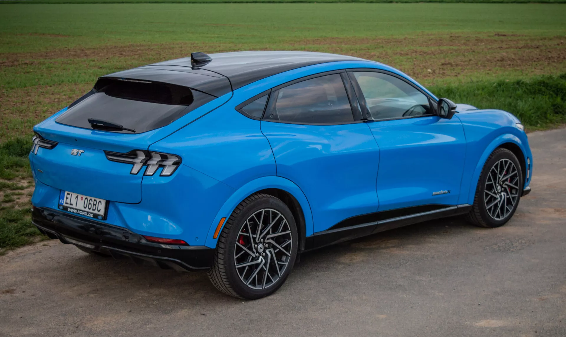 Jasnoniebieskie elektryczne SUV Ford Mustang Mach-E 2020 w dynamicznym widoku z tyłu pod kątem trzech czwartych podkreślającym aerodynamiczny design, eleganckie tylne światła i sportowe koła ze stopu, prezentujący zaawansowaną technologię i napęd elektryczny.