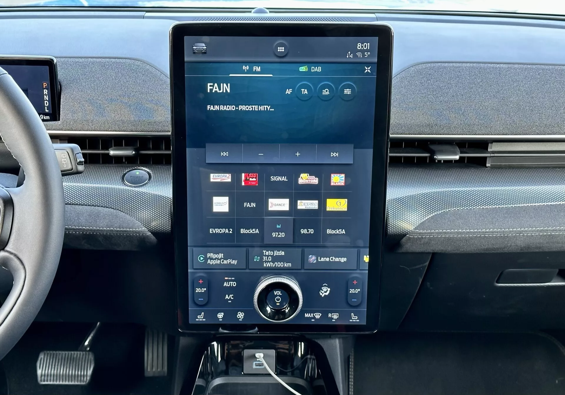 Wewnętrzna konsola centralna Forda Mustang Mach-E 2020 z dużym ekranem dotykowym prezentującym interfejs multimedialny z aplikacjami i ustawieniami, zintegrowane nawiewy powyżej i dodatkowy pokrętło regulacji klimatyzacji poniżej.