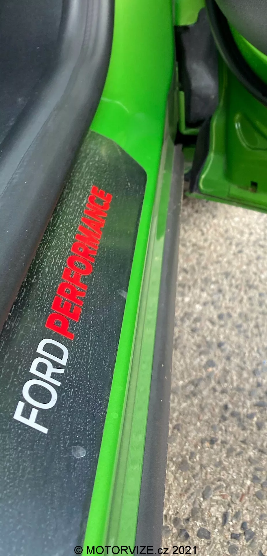 Zbliżenie nakładki progowej Forda Pumy 2020 z napisem 'FORD PERFORMANCE' na tle szczotkowanego metalu, częściowo uchylone drzwi ukazujące żywozielony lakier, podkreślające elementy designu i branding.