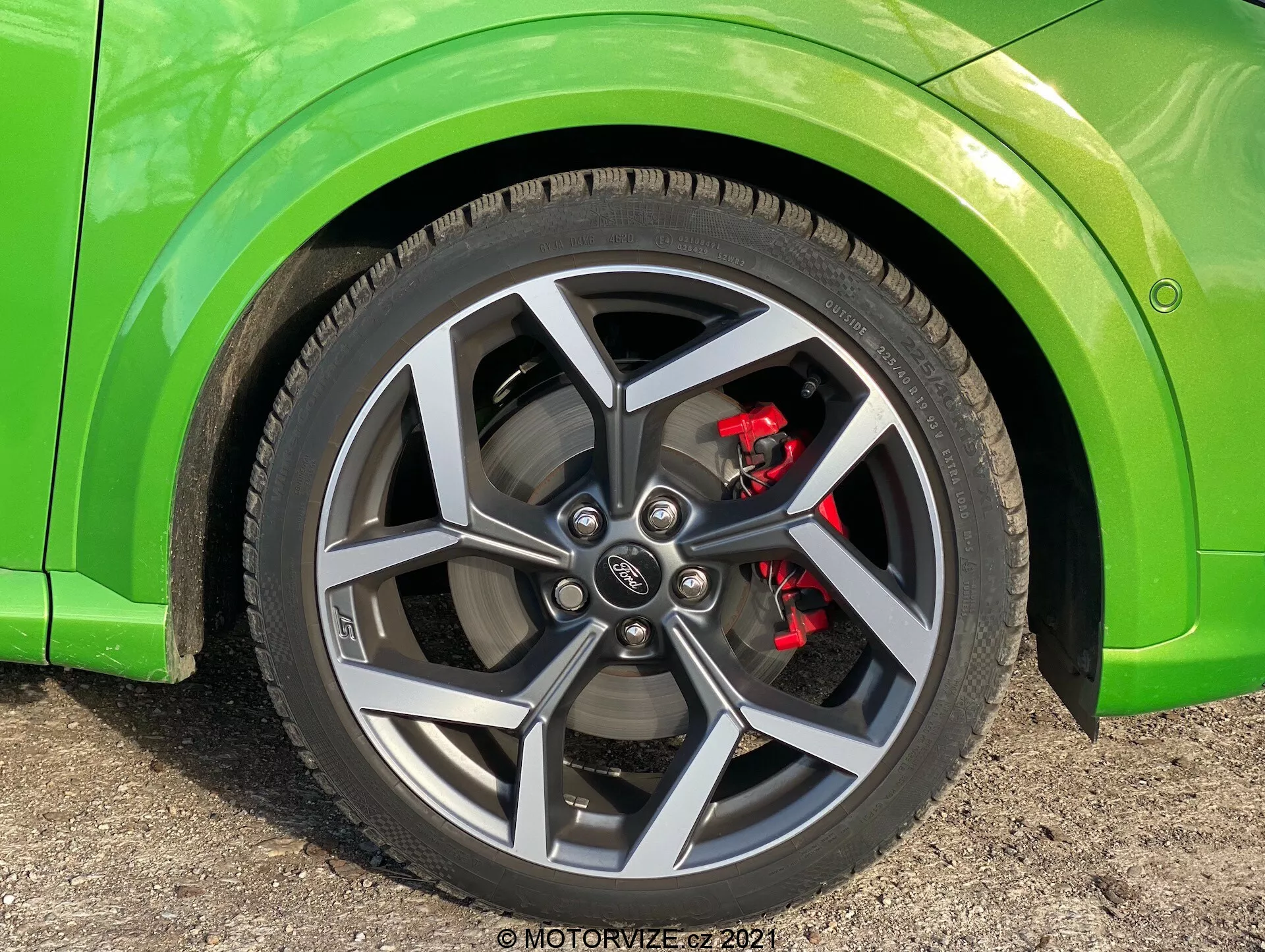 Zbliżenie na koło Ford Puma 2020 z ciemnoszarym, wieloramiennym wzorem, czerwonym zaciskiem hamulcowym, oponą o niskim profilu i nadwoziem w kolorze limonkowym, zrobione z niskiego kąta pokazującym koło prawie na wprost z lekką widocznością boku pojazdu.
