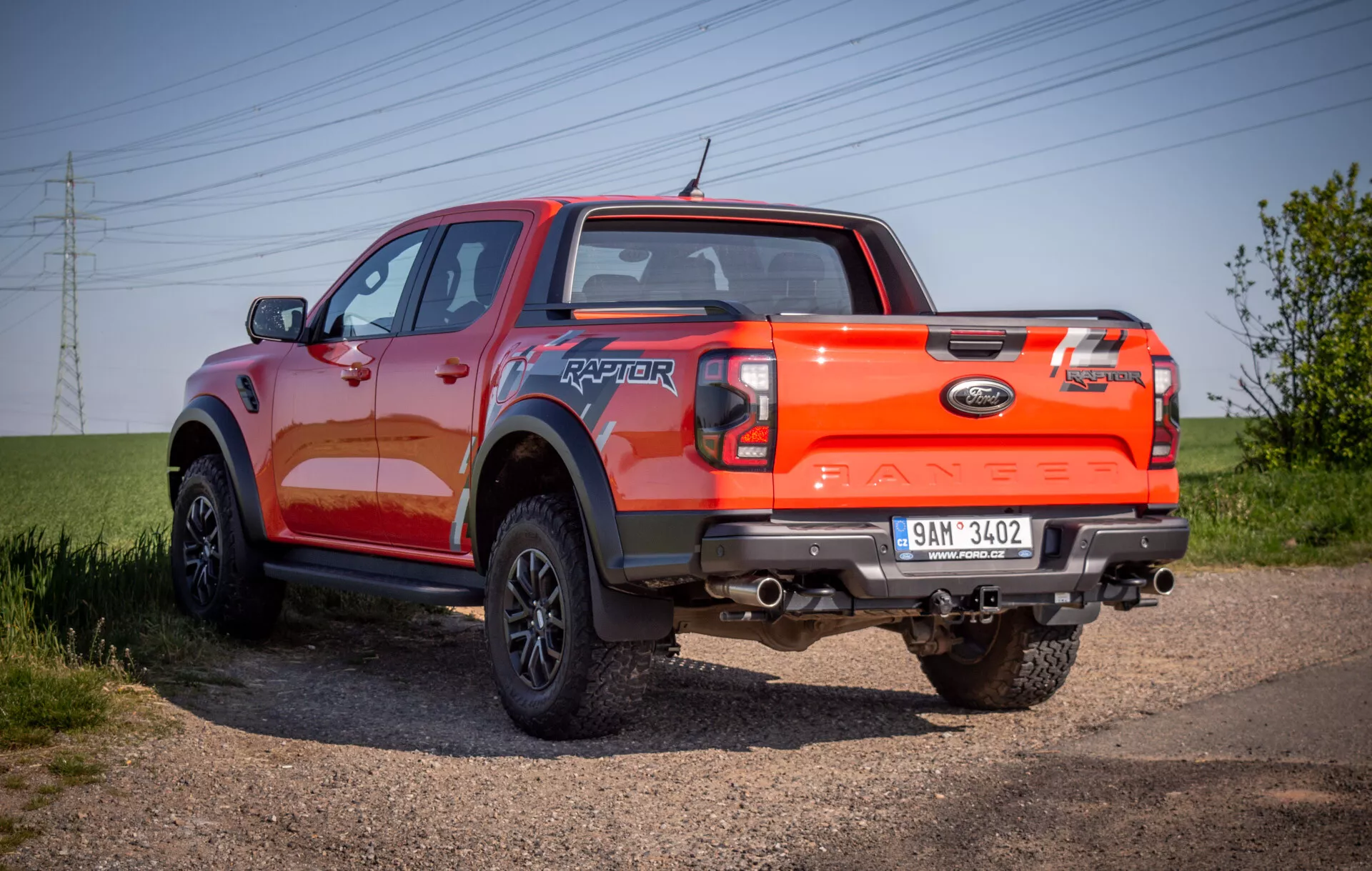 Pickup Ford Ranger Raptor 2022 wyeksponowany na ścieżce żwirowej, prezentujący jego wytrzymały tylny kąt trzy czwarte z naciskiem na zdolności terenowe i jaskrawo pomarańczowe wykończenie lakieru.