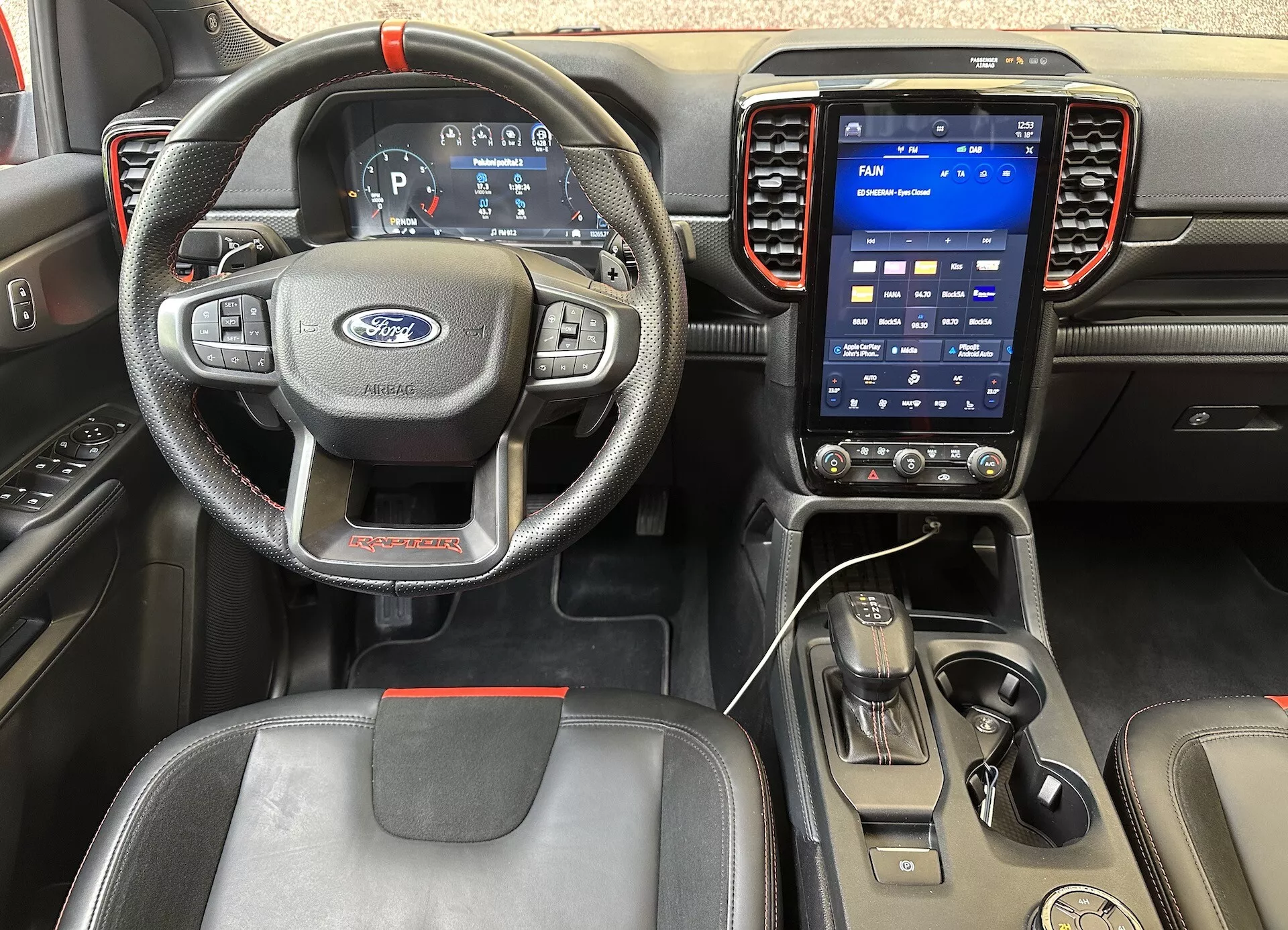 Wnętrze Ford Ranger 2022 z perspektywy kierowcy, pokazujące kierownicę z trzema ramionami z przyciskami, cyfrowy zestaw wskaźników i system informacyjno-rozrywkowy z pionowym ekranem dotykowym na desce rozdzielczej