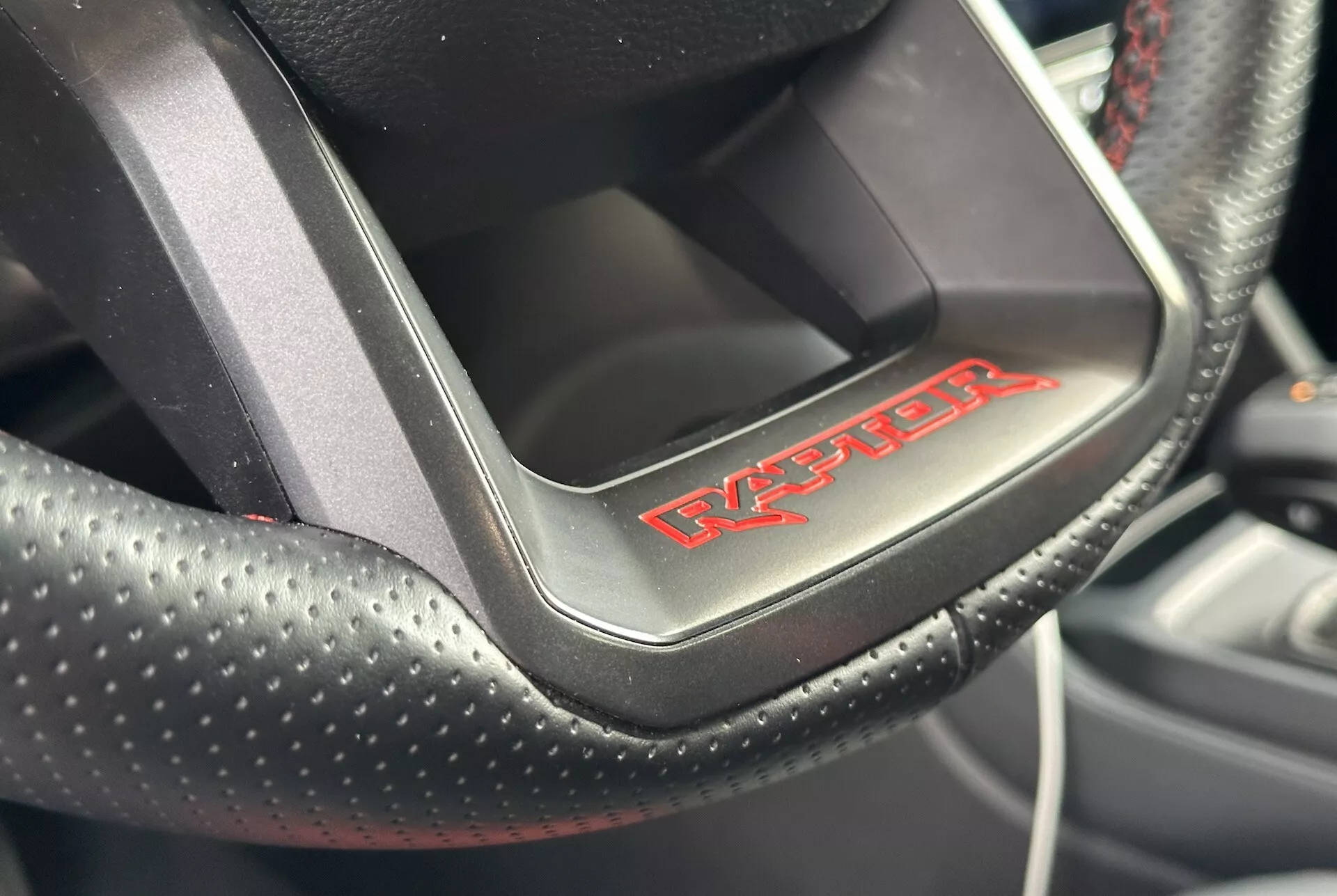 Zbliżenie na kierownicę Dodge Viper prezentującą perforowaną skórę z czerwonymi szwami i odznaką 'Viper', co wskazuje na sportowe, luksusowe wnętrze samochodu.