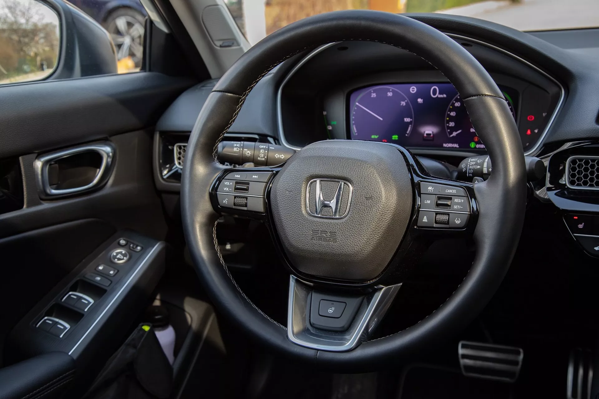 Widok wnętrza Honda Civic 2022 z perspektywy kierowcy, podkreślający wielofunkcyjną kierownicę obszytą skórą, cyfrowy kokpit, część konsoli środkowej z ekranem dotykowym oraz kontrole na drzwiach kierowcy do kompleksowego wyświetlenia nowoczesnych funkcji technologicznych i luksusowego designu pojazdu.