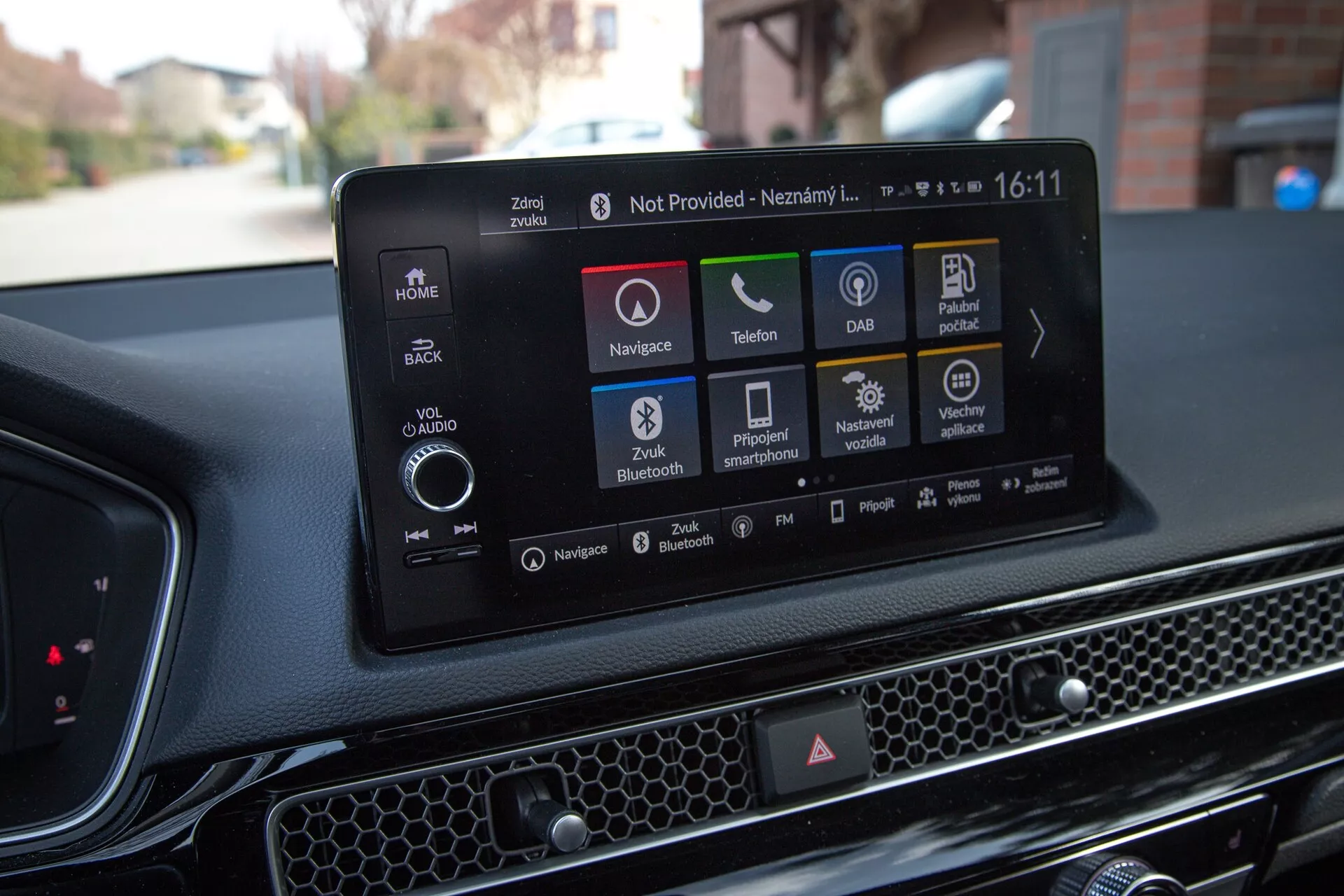 Wnętrze Hondy Civic 2022 pokazujące nowoczesny system informacyjno-rozrywkowy z ekranem dotykowym z nawigacją, ikonami odtwarzania audio i mediów, łącznością telefoniczną, DAB, informacjami o stanie samochodu, opcjami Bluetooth i ustawieniami pojazdu, na tle teksturowego deski rozdzielczej z wzorem plaster miodu.