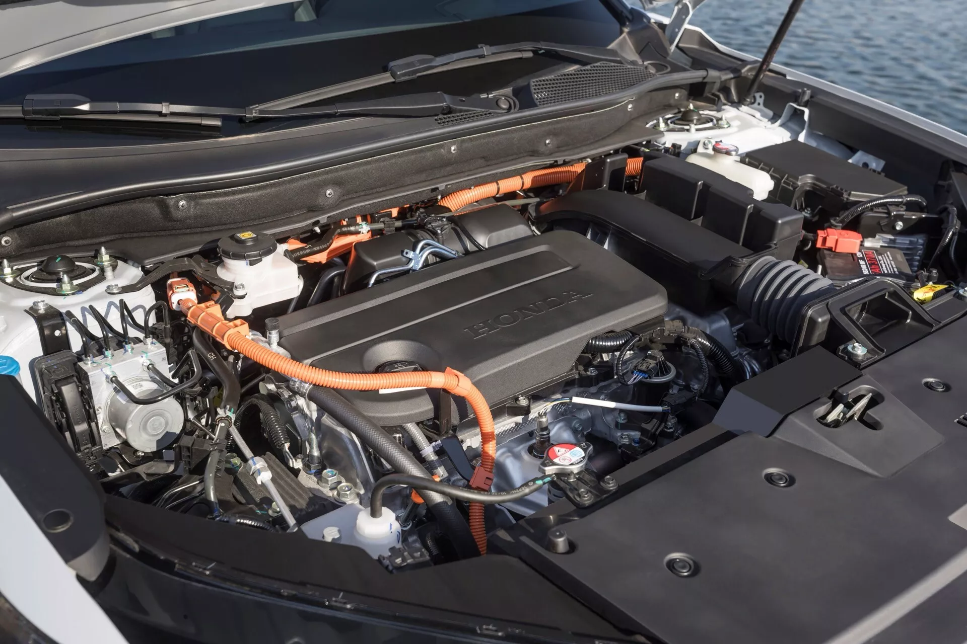 Zbliżenie na hybrydowy silnik i komponenty Hondy CR-V 6. generacji 2023, z wysokonapięciowymi kablami i pokrywą silnika oznaczoną przez Toyotę, pokazujące połączenie technologii pojazdów spalinowych i elektrycznych