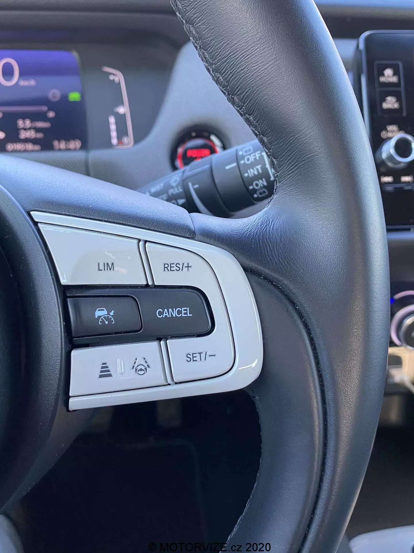 Szczegółowy widok na elementy sterujące na kierownicy Honda Jazz 2020 Crosstar, koncentrujący się na przyciskach i funkcjach po lewej stronie, takich jak LIM (ogranicznik prędkości), RES/+ (wznowienie lub zwiększenie prędkości), CANCEL oraz SET/- (ustawianie lub zmniejszanie prędkości). Obraz jest wykonany z perspektywy kierowcy, podkreślając czarną skórzaną kierownicę z matowym i połyskującym wykończeniem oraz pokazując ikony związane z tempomatem i możliwymi zaawansowanymi systemami wspomagania kierowcy.