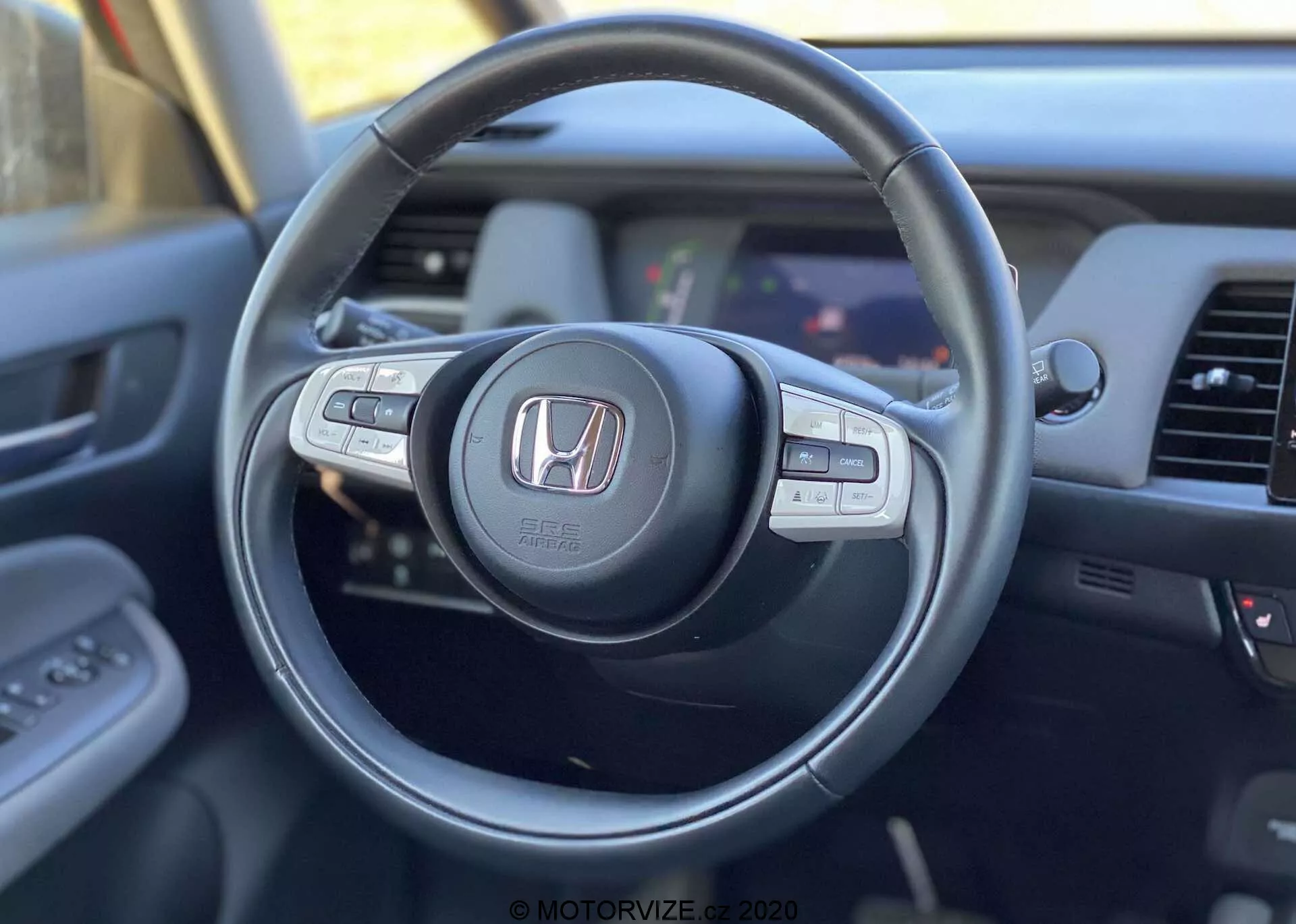 Widok wnętrza Hondy Jazz Crosstar 2020 z perspektywy kierowcy, skupiony na nowoczesnej kierownicy z logo Honda, wyposażonej w wielofunkcyjne przyciski do sterowania audio, tempomatem i rozmowami bez użycia rąk, z częściowym widokiem na deskę rozdzielczą i system informacyjno-rozrywkowy.