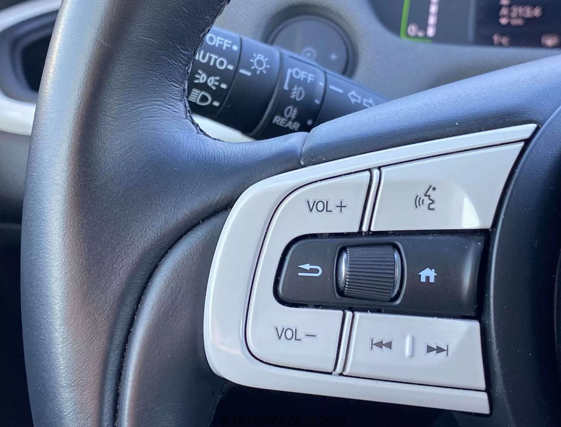 Zbliżenie na zamontowane na kierownicy kontrolki Honda Jazz Crosstar 2020, pokazujące regulację głośności, system telefonu głośnomówiącego i przyciski możliwego sterowania tempomatem lub wyborem ścieżek audio. Centralne skupienie na kierownicy obitej skórą z srebrnym wykończeniem podkreślającym komfort i elegancki wygląd.