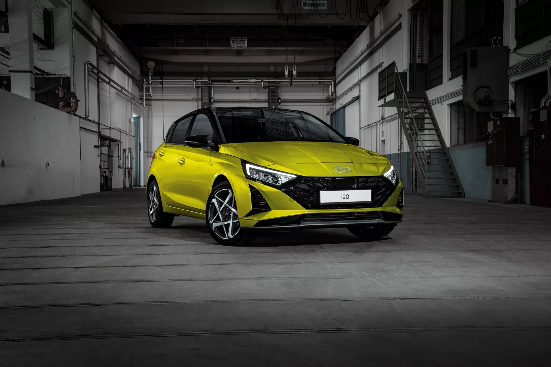 Hyundai i20 2023 (lifting 3. generacji) z widoku trzy czwarte przedniego, prezentujący nowoczesny design hatchbacka, reflektory LED, sportowy przedni zderzak i felgi ze stopu wewnątrz przemysłowego magazynu z betonową podłogą i metalowymi drzwiami
