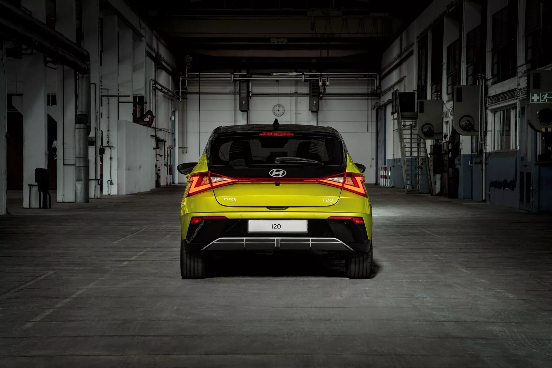 Tylny widok hatchbacka Hyundai i20 2023 (3. generacja-facelifting) z tylnymi światłami LED i asystą parkingową, wyróżniony w przemysłowym otoczeniu