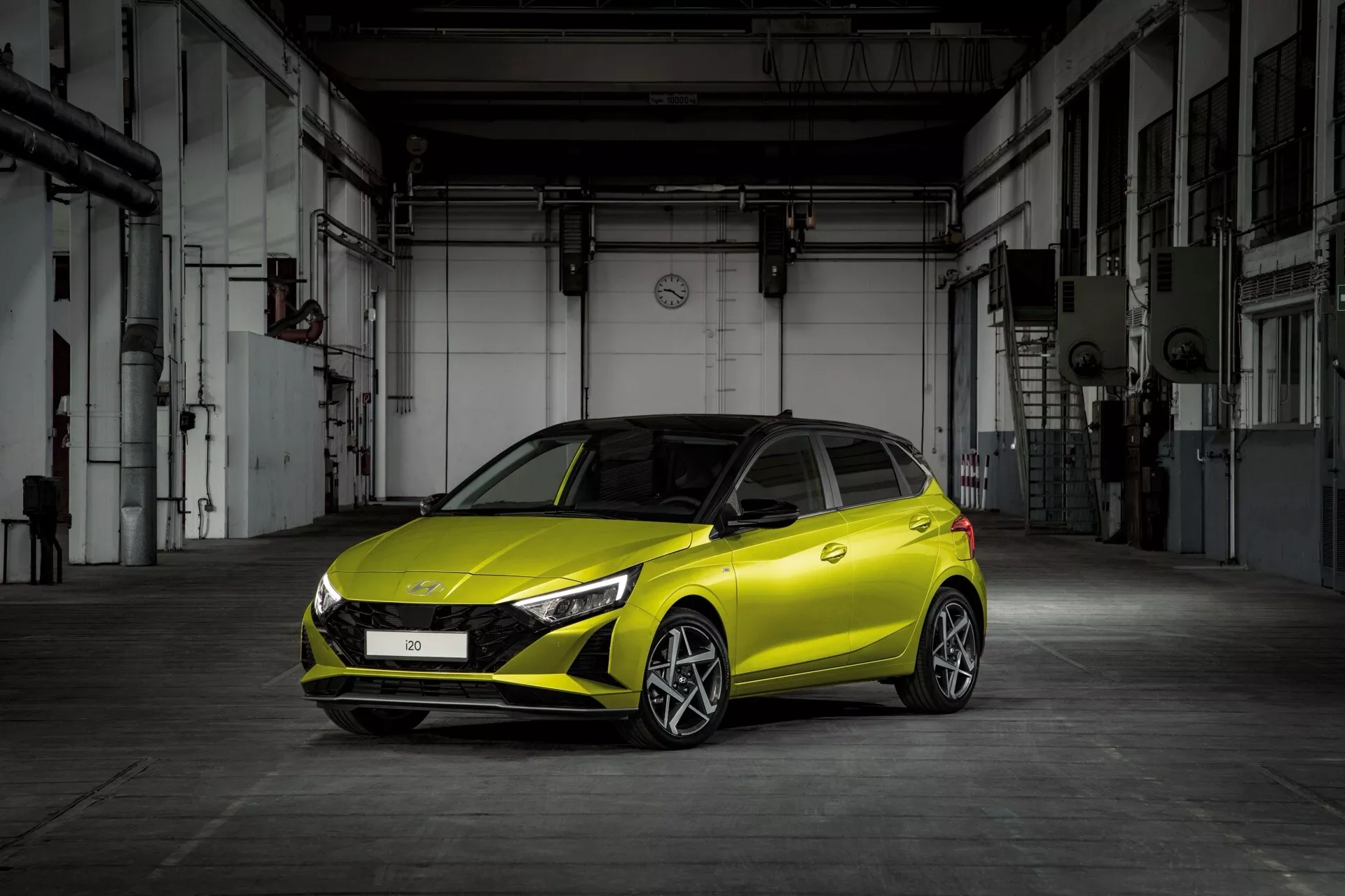 Hyundai i20 3. generacja po liftingu, rok 2023, sfotografowana z przodu pod kątem trzech czwartych, prezentująca eleganckie reflektory LED, sportową atrapę chłodnicy i żywy żółty kolor na tle industrialnym, podkreślając jej nowoczesny design i cechy technologiczne.