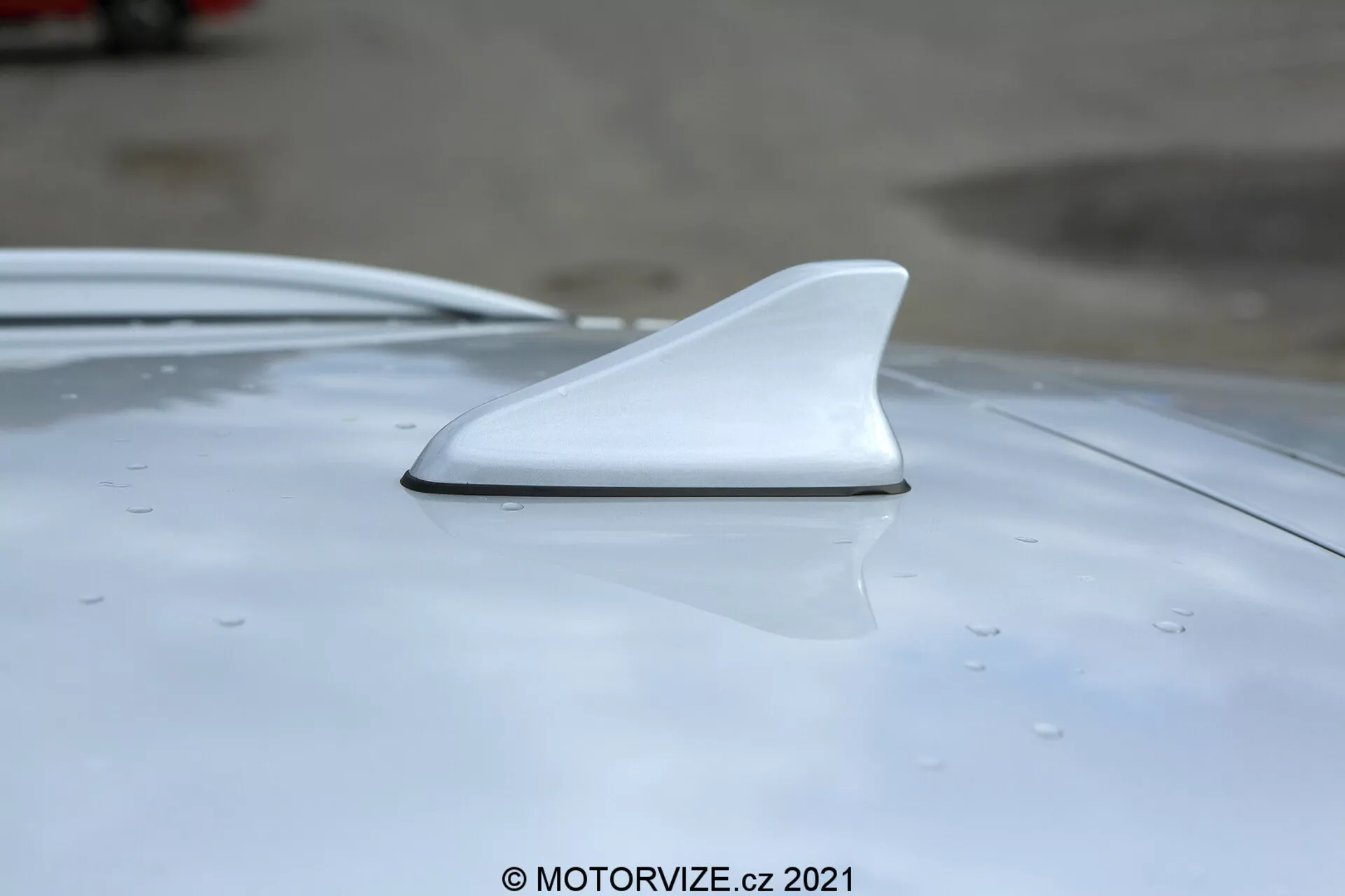 Zbliżenie anteny w kształcie płetwy rekina zamontowanej na dachu białego Hyundai i30 2020, pokazujące jej aerodynamiczny design z bocznego i lekko podniesionego kąta z naciskiem na gładką integrację i widoczne krople sugerujące niedawny deszcz lub mycie.