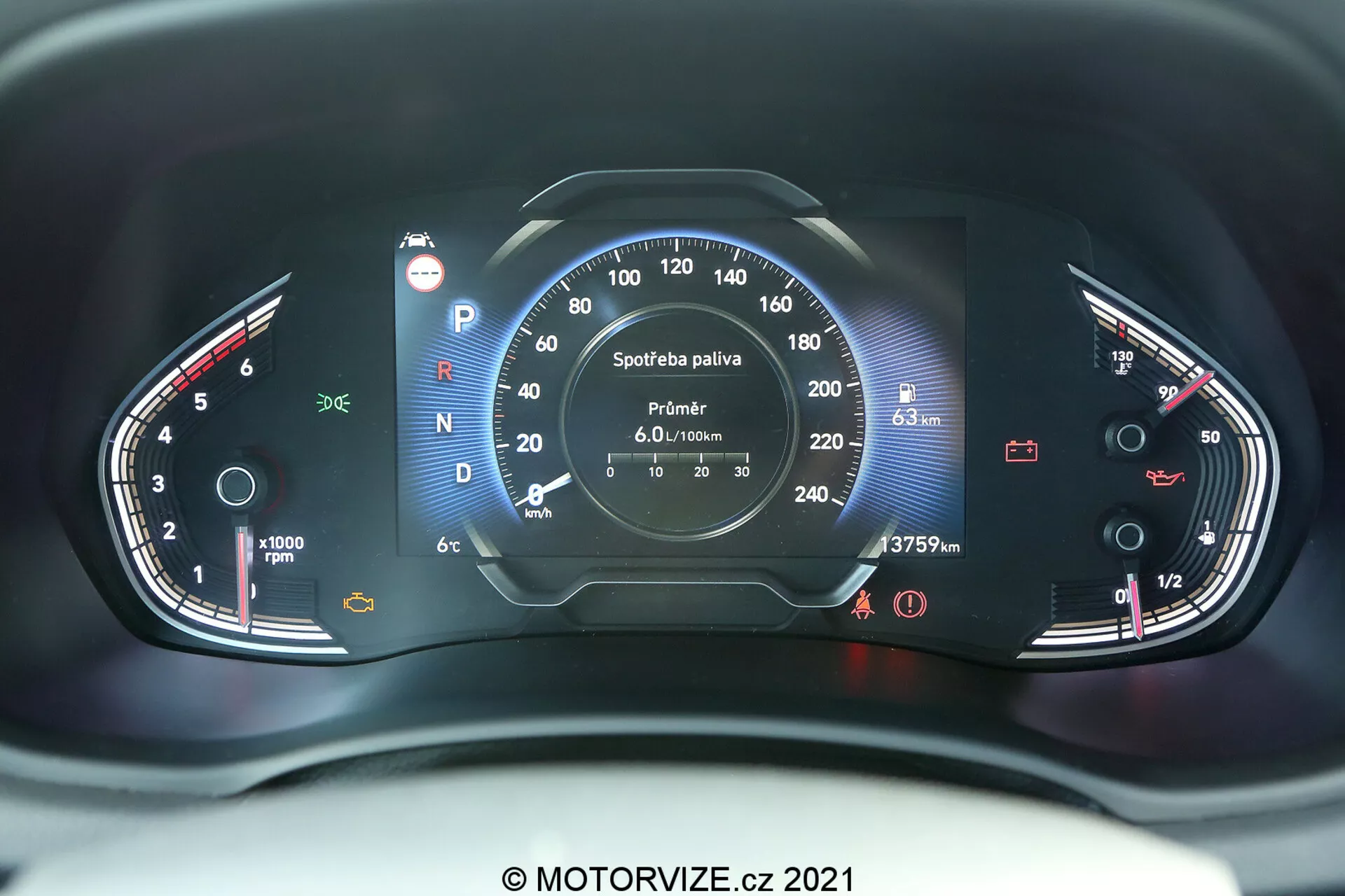 Zbliżenie na panel wskaźników Hyundai i30 2020 z perspektywy fotela kierowcy. Zdjęcie wykonano pod kątem centralnym, ukazując zarówno analogowe, jak i cyfrowe elementy. Lewa strona zawiera obrotomierz sięgający do 8000 obrotów na minutę z małym wskaźnikiem temperatury. Prawa strona zawiera prędkościomierz mierzący prędkość do 260 km/h i wskaźnik paliwa. Centralny wyświetlacz cyfrowy pokazuje informacje takie jak wybór biegu (obecny bieg to Park), odczyt licznika kilometrów (37579 km), cyfrowy prędkościomierz (---- km/h) i szczegóły komputera pokładowego dotyczące zużycia paliwa i pozostałego zasięgu. Tablica rozdzielcza jest oświetlona czerwonymi i białymi światłami, co poprawia widoczność i nie zakłóca widzenia nocnego. Na obrazie widoczny jest znak wodny 'MOTORVIZE.cz 2021'.