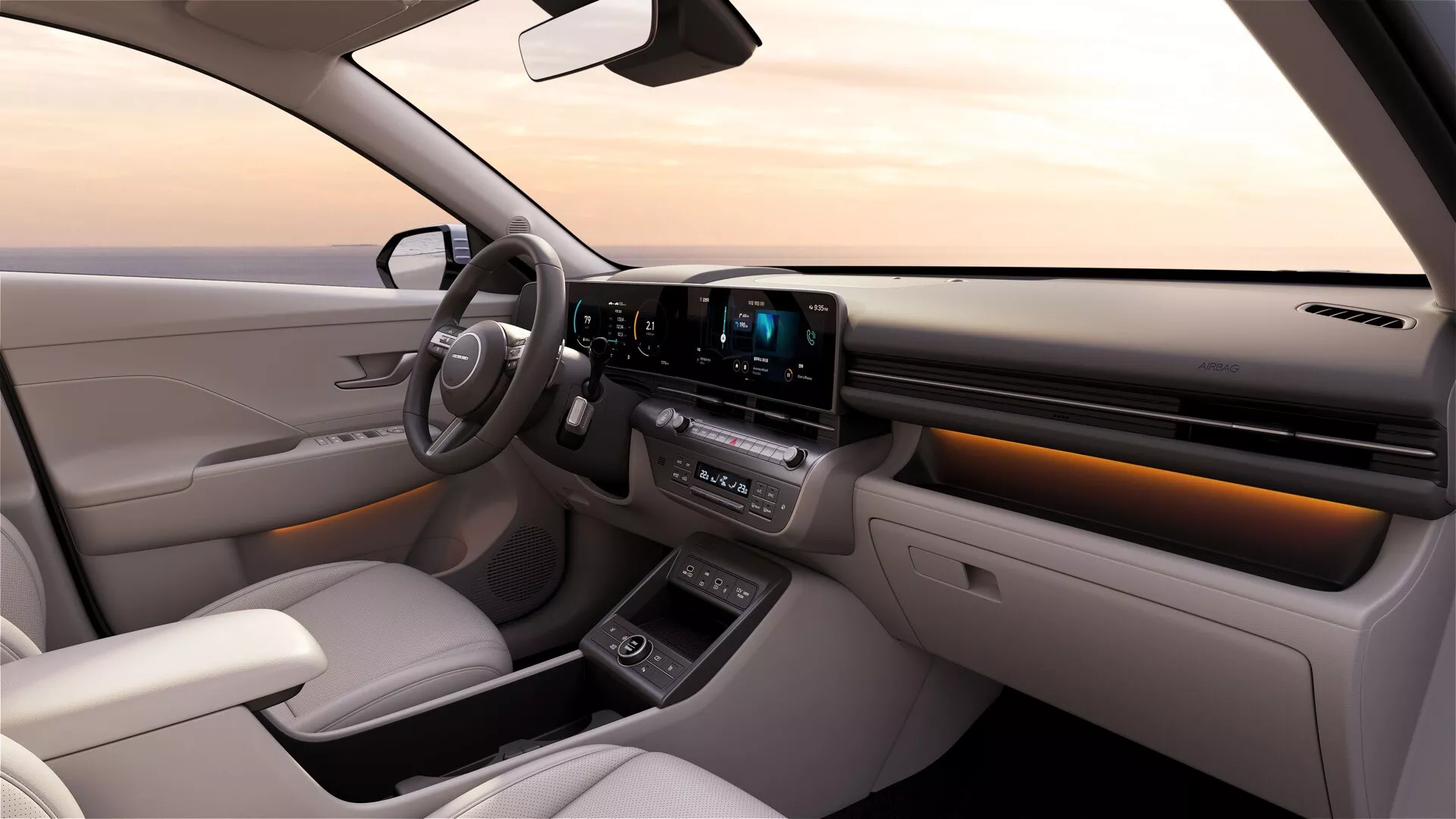 Widok wnętrza Hyundai Kona 2023 z perspektywy tylnej części kabiny w kierunku deski rozdzielczej prezentujący cyfrowy zespół wskaźników, duży ekran dotykowy systemu infotainment, system kontroli klimatu, selektor biegów przyciskowy oraz oświetlenie ambientowe