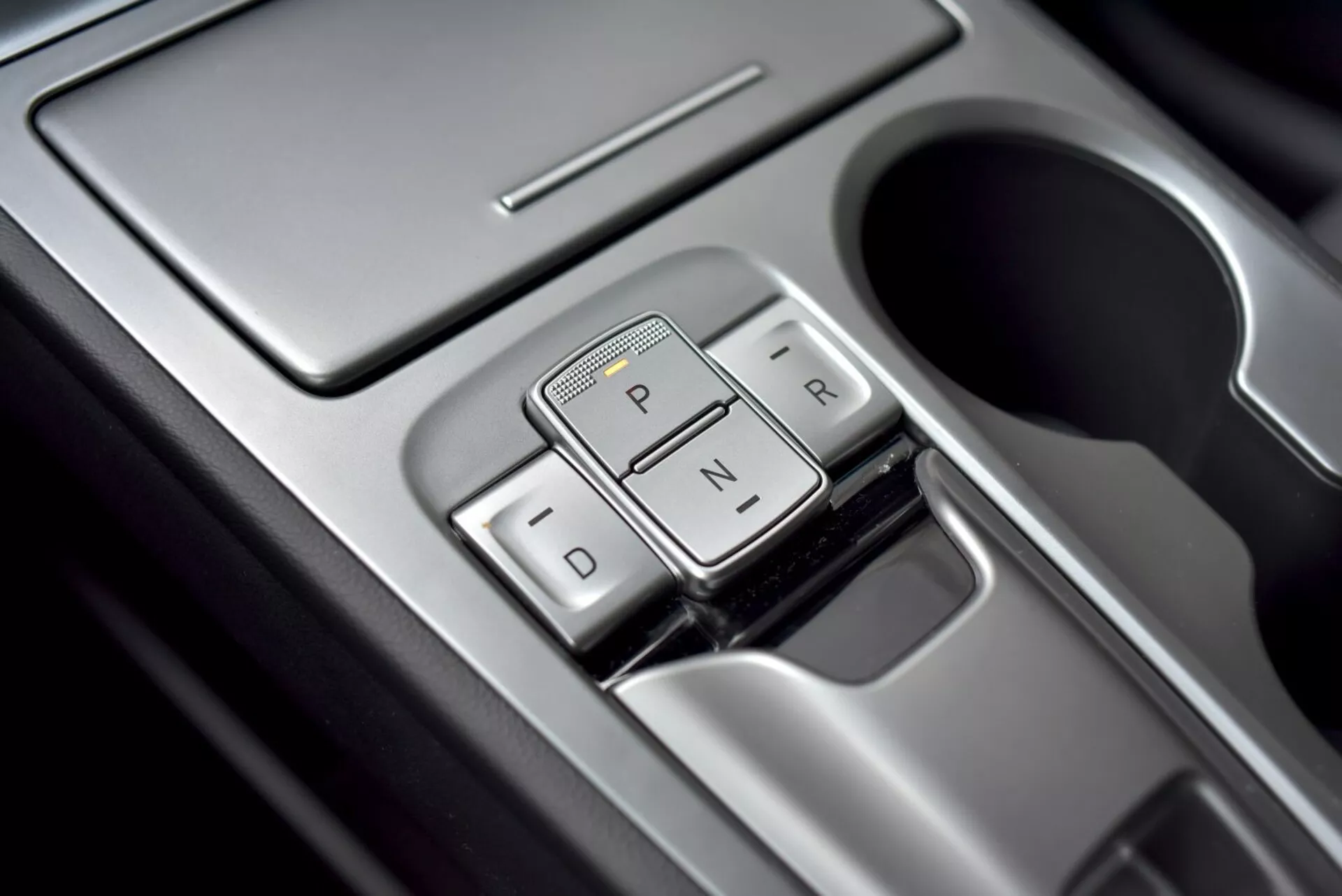 Zbliżenie na wybierak biegów automatycznej skrzyni biegów Hyundai Kona 2021 o eleganckim wyglądzie, z oznaczeniami 'P', 'R', 'N', 'D' i wykończeniem premium, widok z góry