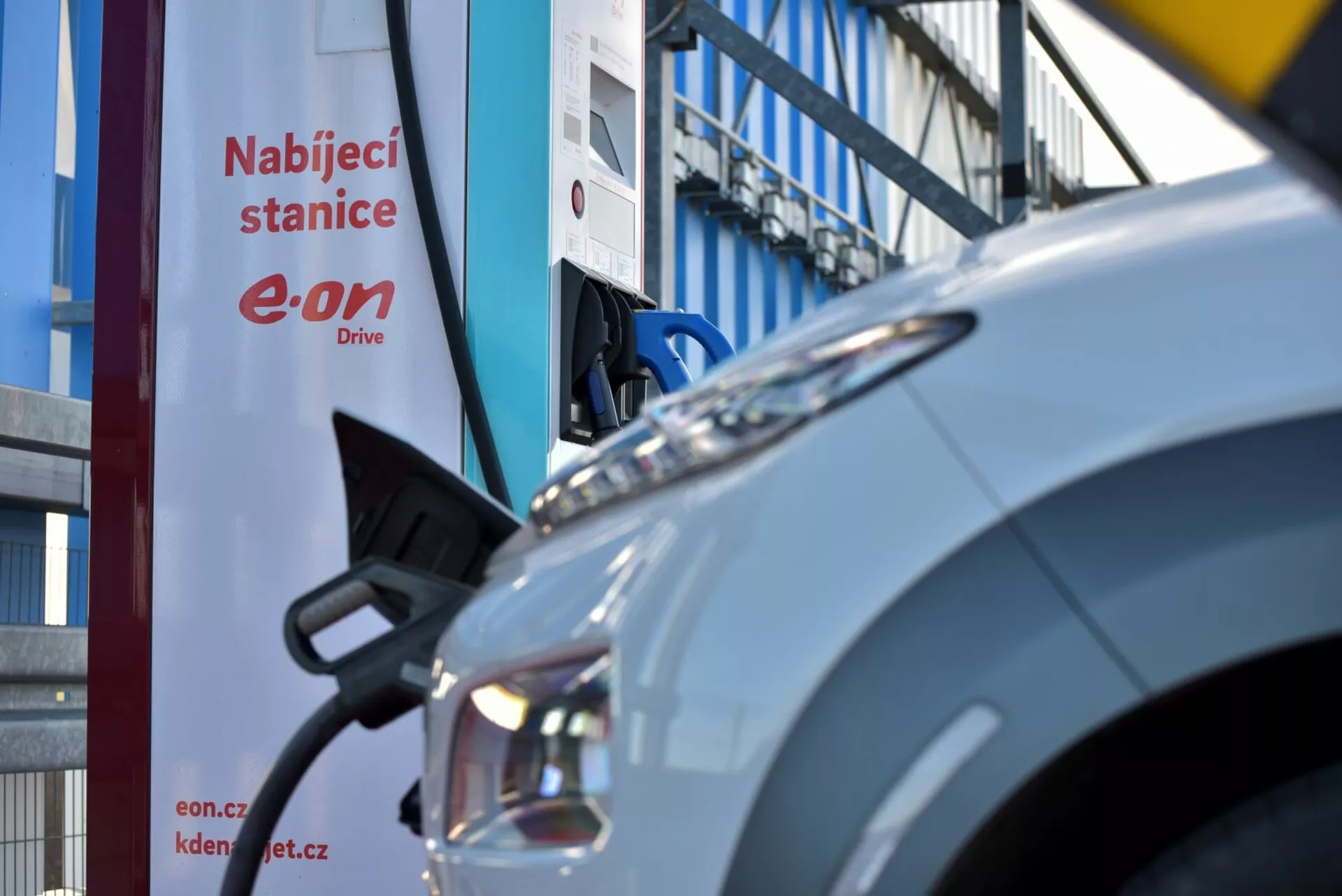 Elektryczny Hyundai Kona 2021 zaparkowany przy stacji ładowania, pokazujący przedni błotnik, zespół reflektorów i port ładowania, z częściowo widocznym znakiem 'Nabíjecí stanice'