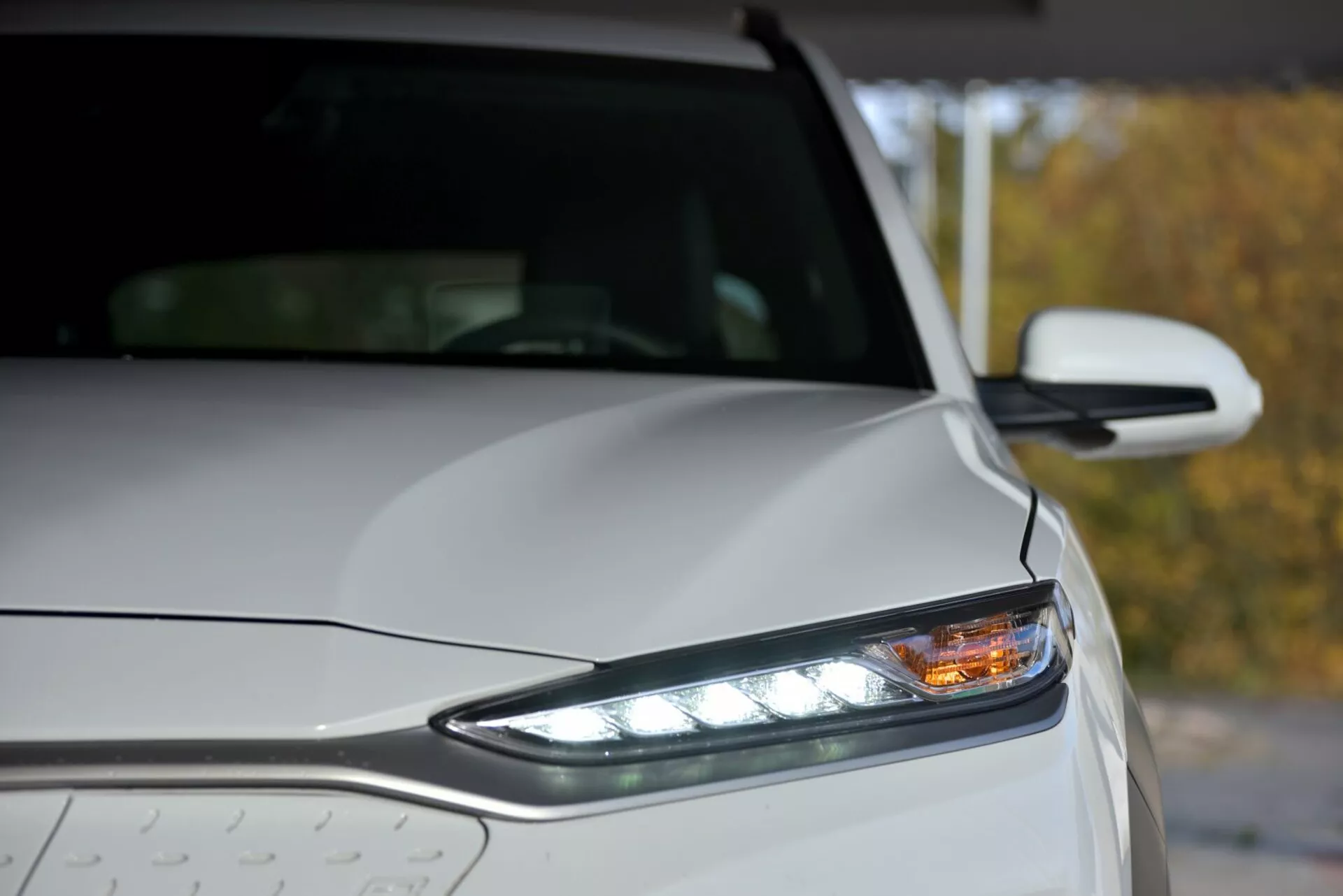 Zbliżenie na lewą przednią część Hyundai Kona Elektro 2021 z reflektorem LED, światłami do jazdy dziennej i kroplami deszczu na metalicznym nadwoziu