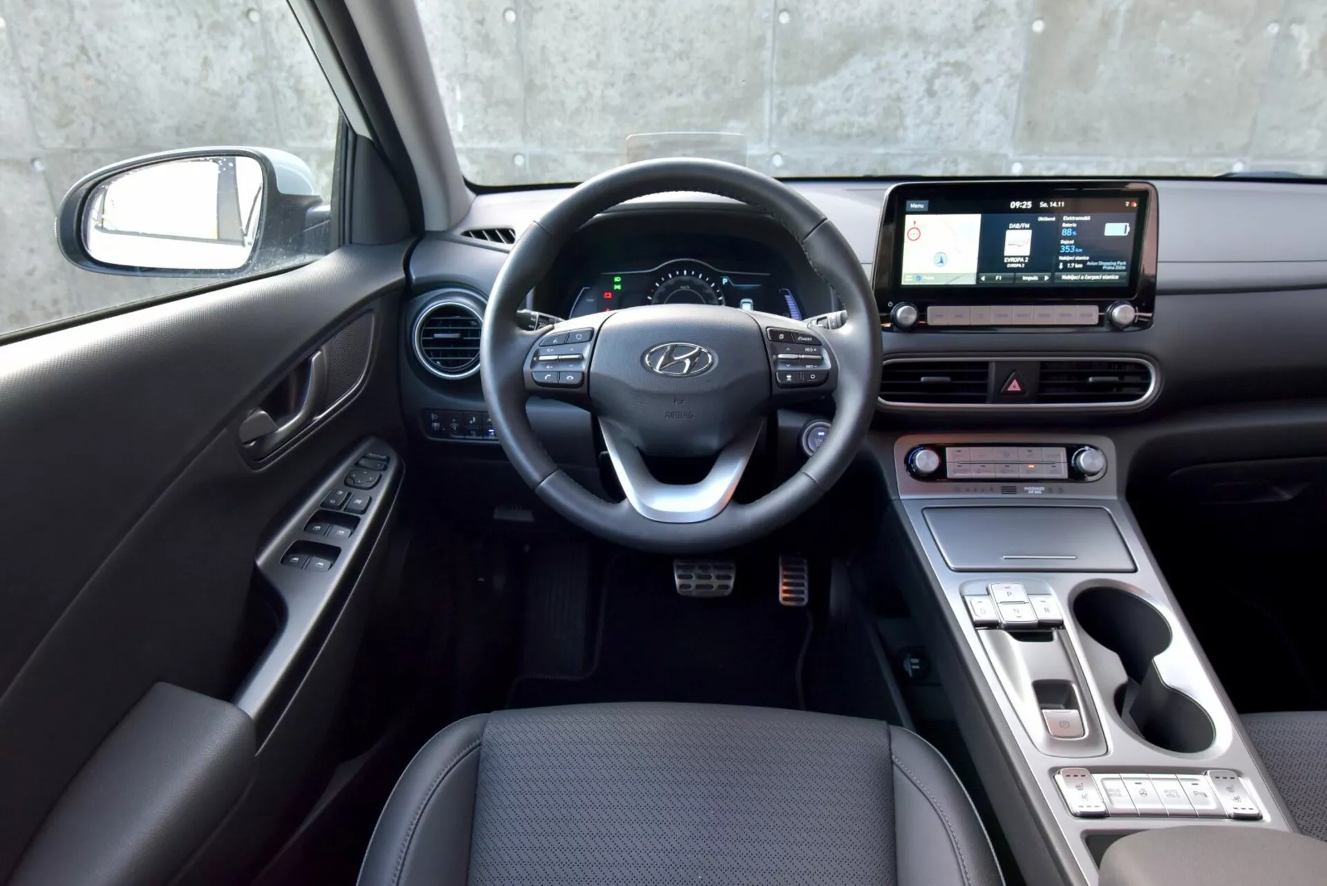 Wnętrze Hyundai Kona Electric 2021 z perspektywy kierowcy z widoczną kierownicą, zestawem wskaźników, ekranem dotykowym systemu rozrywki, pokrętłami kontrolnymi klimatyzacji i selektorem biegów