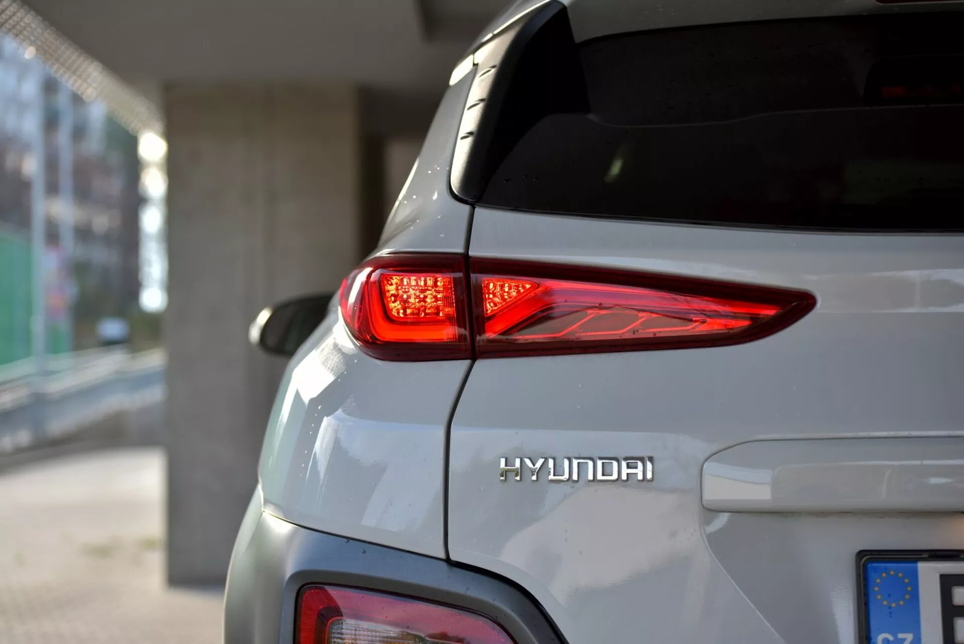Zbliżony widok na tylną prawą stronę Hyundai Kona Electric 2021, podkreślający zakrzywione tylne światło LED, logo Hyundai i elegancką srebrną karoserię pod naturalnym oświetleniem