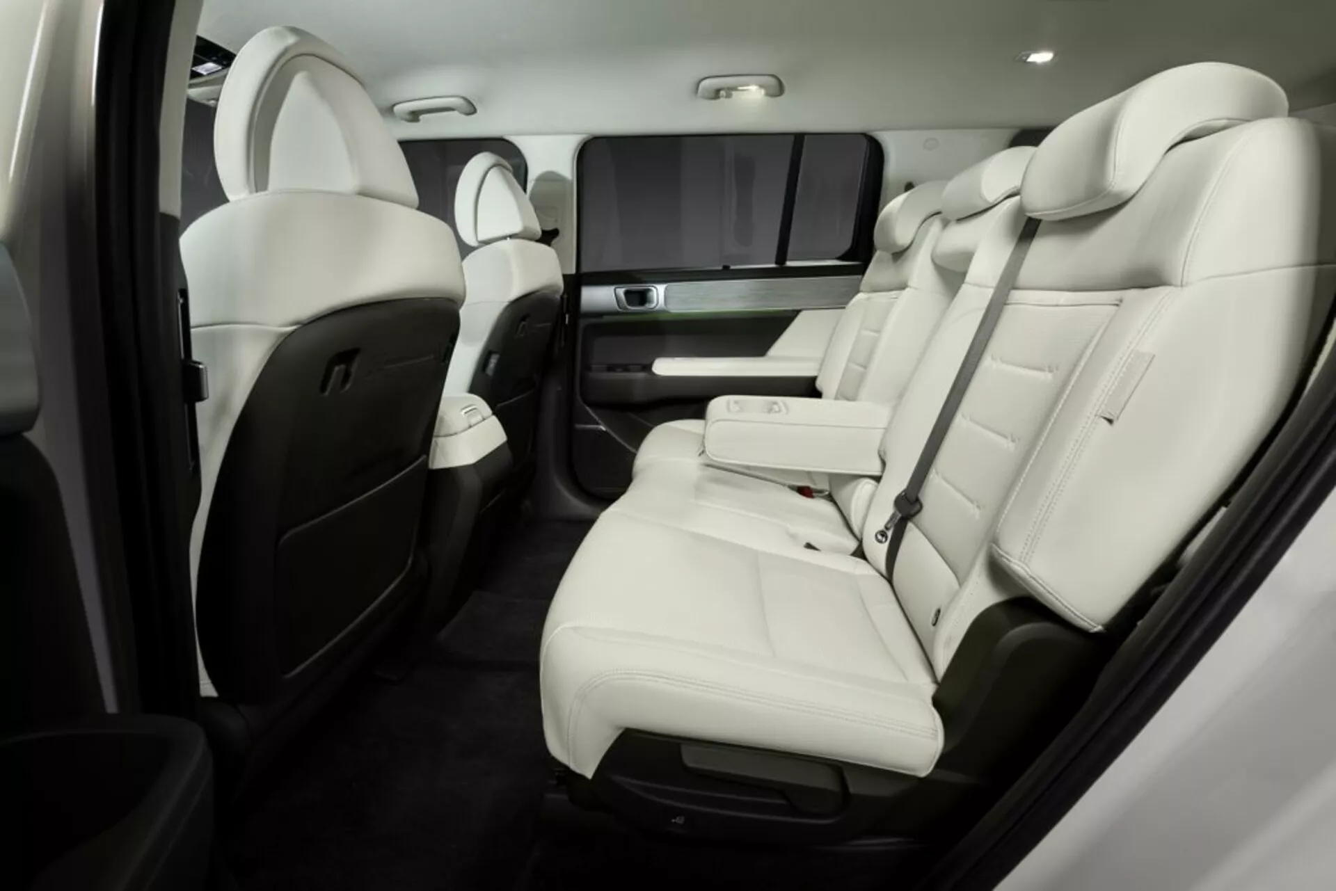 Luksusowe wnętrze Hyundai Santa Fe 2024 (5. generacja) z naciskiem na tylne siedzenia pasażerów. Jasnokolorowe skórzane fotele z kontrastującymi akcentami, składany podłokietnik środkowy z uchwytami na kubki, system rozrywki dla pasażerów tylnych siedzeń oraz zaawansowane sterowanie klimatyzacją i regulacją foteli. Wysokiej jakości materiały i kunszt wykonania zwiększają uczucie luksusu.