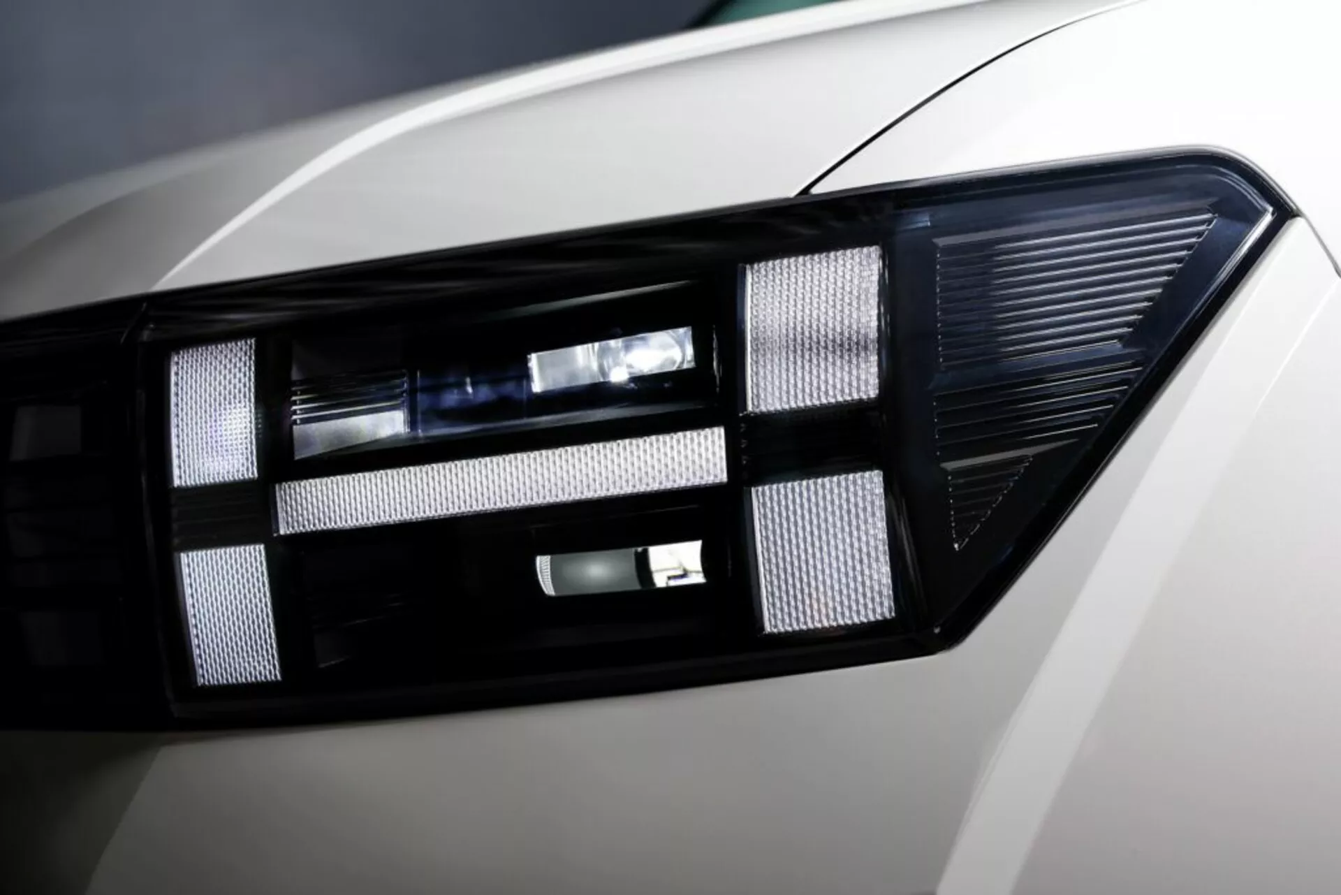 Zbliżenie nowoczesnego zespołu reflektorów Hyundai Santa Fe 2024 (5. generacja), prezentujące zaawansowaną technologię oświetlenia LED/HID, elegancki design, soczewkę projektora i błyszczące wykończenie nadwozia.