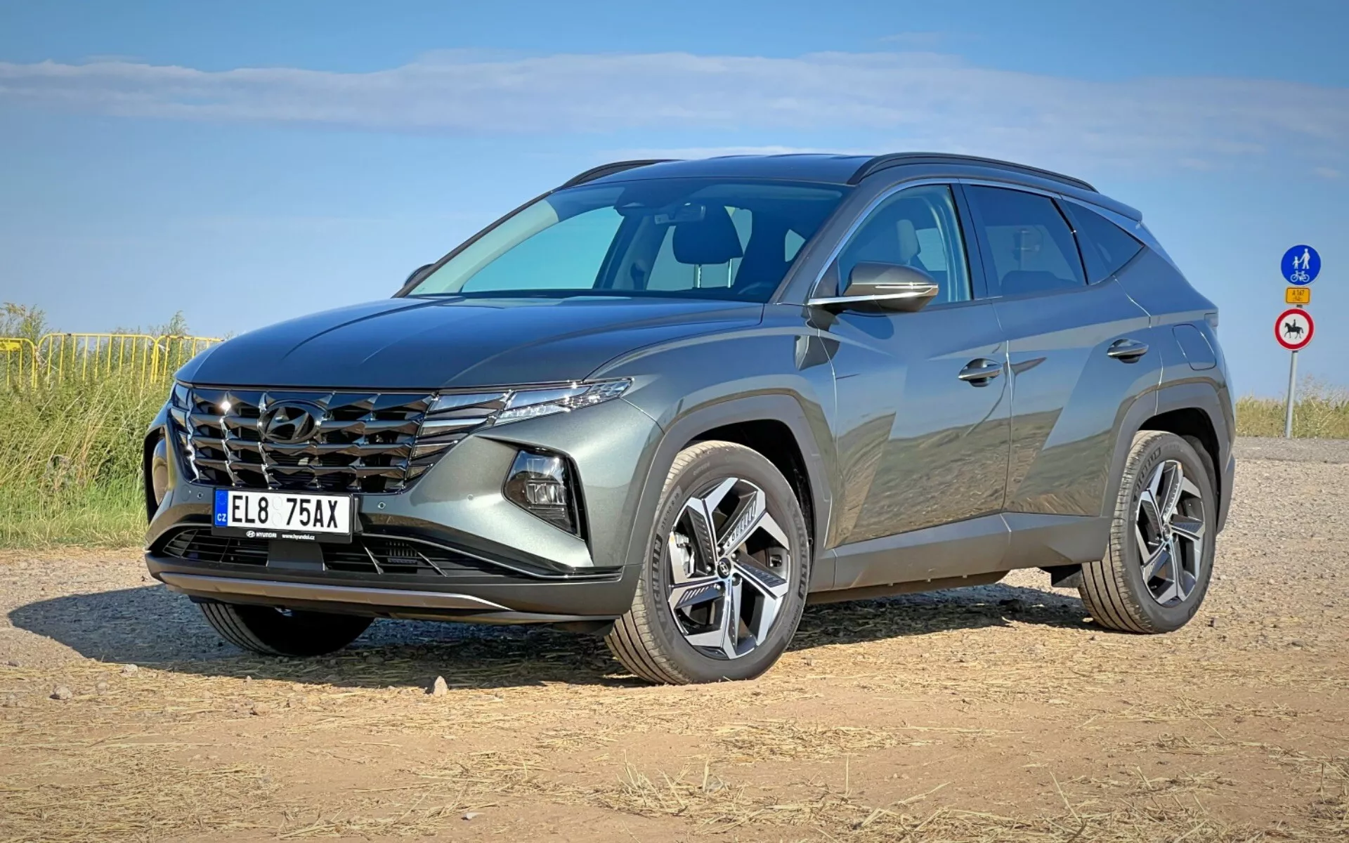 Nowoczesne SUV Hyundai Tucson 2020 pokazane z przodu pod kątem trzech kwart, prezentujące charakterystyczną kratkę, eleganckie reflektory, przednią część, wyrzeźbioną maskę i felgi aluminiowe na poboczu gruntowym pod czystym niebem