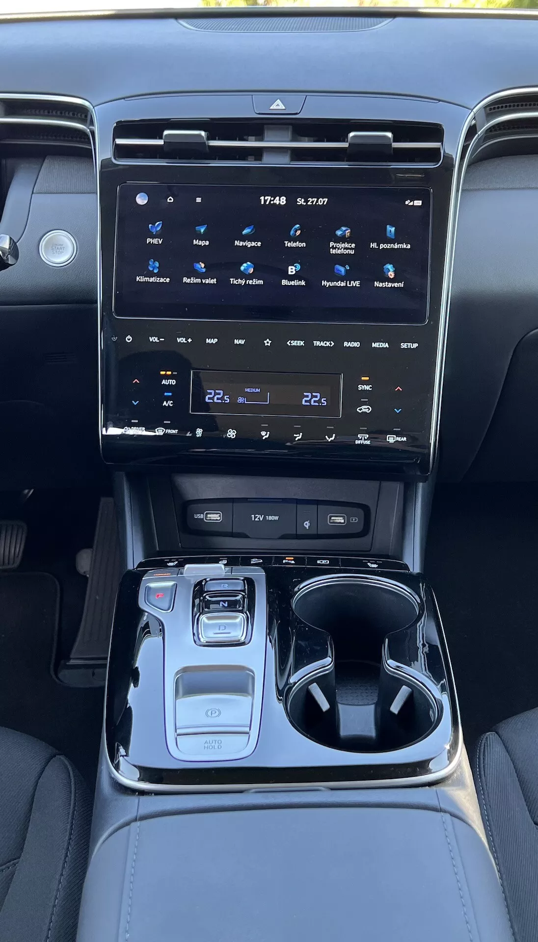 Wnętrze Hyundai Tucson 2020 prezentujące konsolę środkową z dużym systemem infotainment z ekranem dotykowym, przyciski kontroli klimatyzacji, elektronicznym selektorem biegów, selektorem trybu jazdy, uchwyty na kubki, przegródką na drobiazgi i oświetleniem ambient.