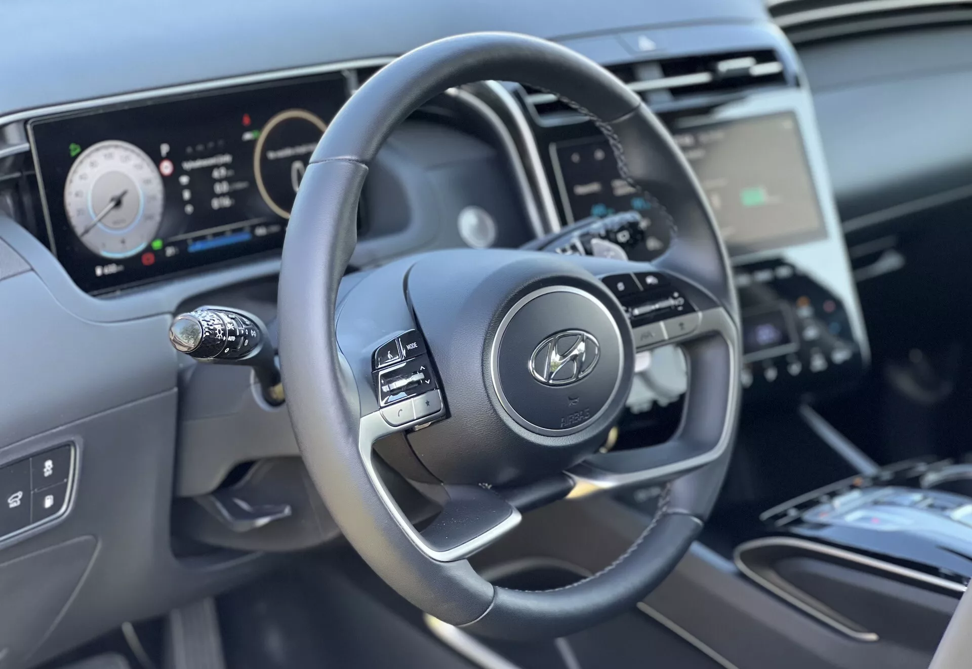 Widok wnętrza Hyundai Tucson 2020 skupiający się na kierownicy i cechach deski rozdzielczej z perspektywy kierowcy, podkreślający trójramienny projekt z przyciskami sterowania, cyfrowy zespół wskaźników oraz częściowy widok na konsolę środkową i sterowanie klimatyzacją.