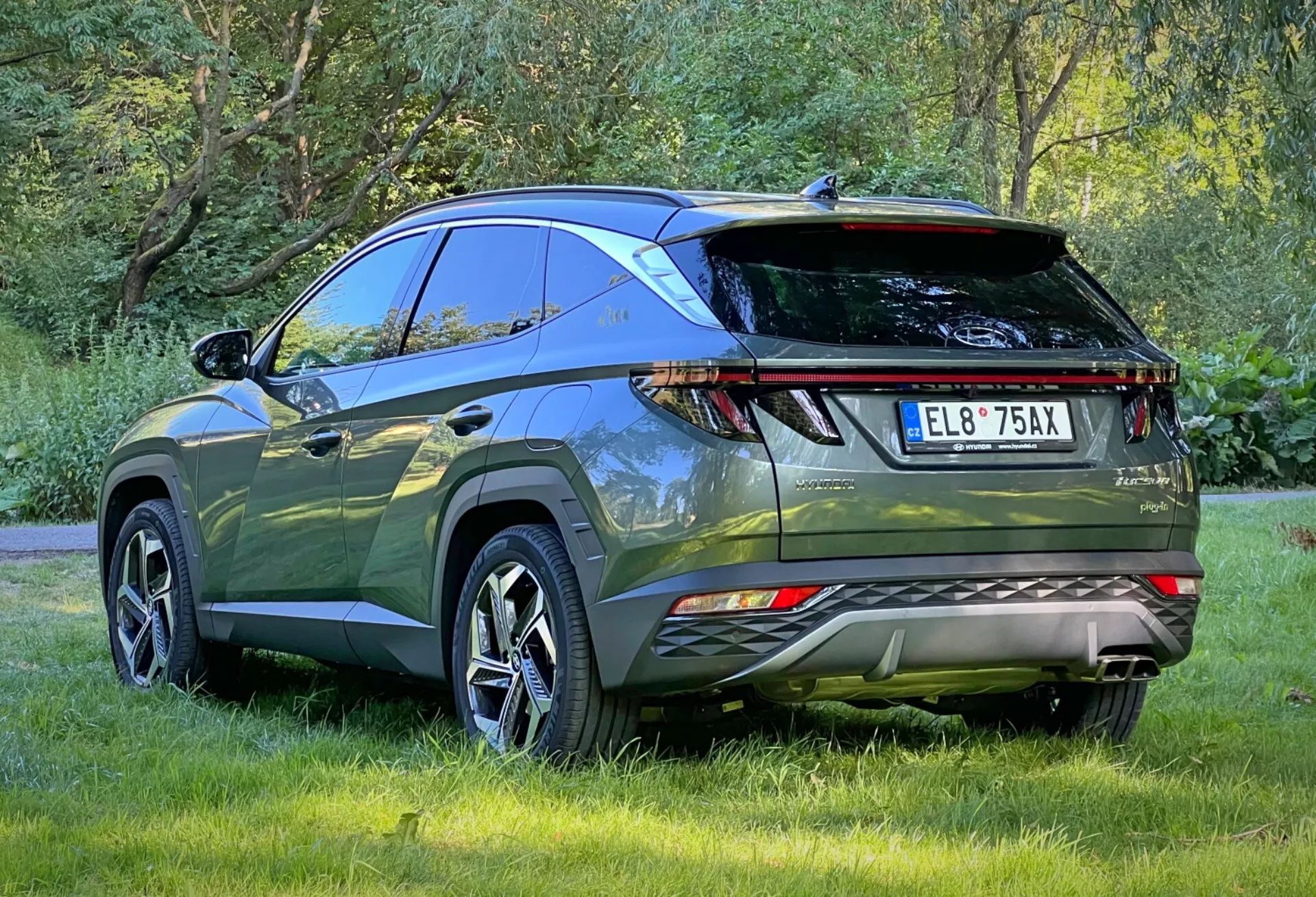 Tylny trzykwartalny widok Hyundai Tucson 2020 podkreślający diodowe tylne światła, czujniki parkowania, podwójne rury wydechowe, sportowy spoiler tylny i relingi dachowe, zaparkowany na zewnątrz na trawie, ukazujący aerodynamiczny design i zaawansowane funkcje nowoczesnego SUV-a crossovera do przygód na świeżym powietrzu i praktycznego użytkowania.