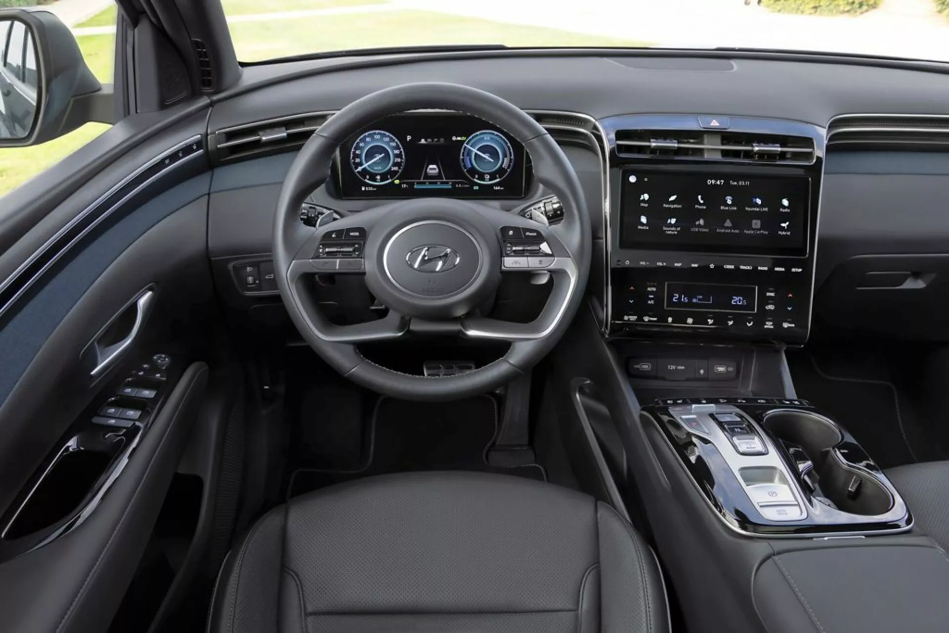 Widok wnętrza Hyundai Tucson 2020 z perspektywy kierowcy, podkreślający deskę rozdzielczą, wielofunkcyjną kierownicę z logo Hyundai, w pełni cyfrowy panel instrumentów, wertykalny system infotainment z ekranem dotykowym, minimalistyczne sterowanie na konsoli centralnej, elektroniczny selektor biegów, tapicerkę skórzaną i wyszukane monochromatyczne schematy kolorów