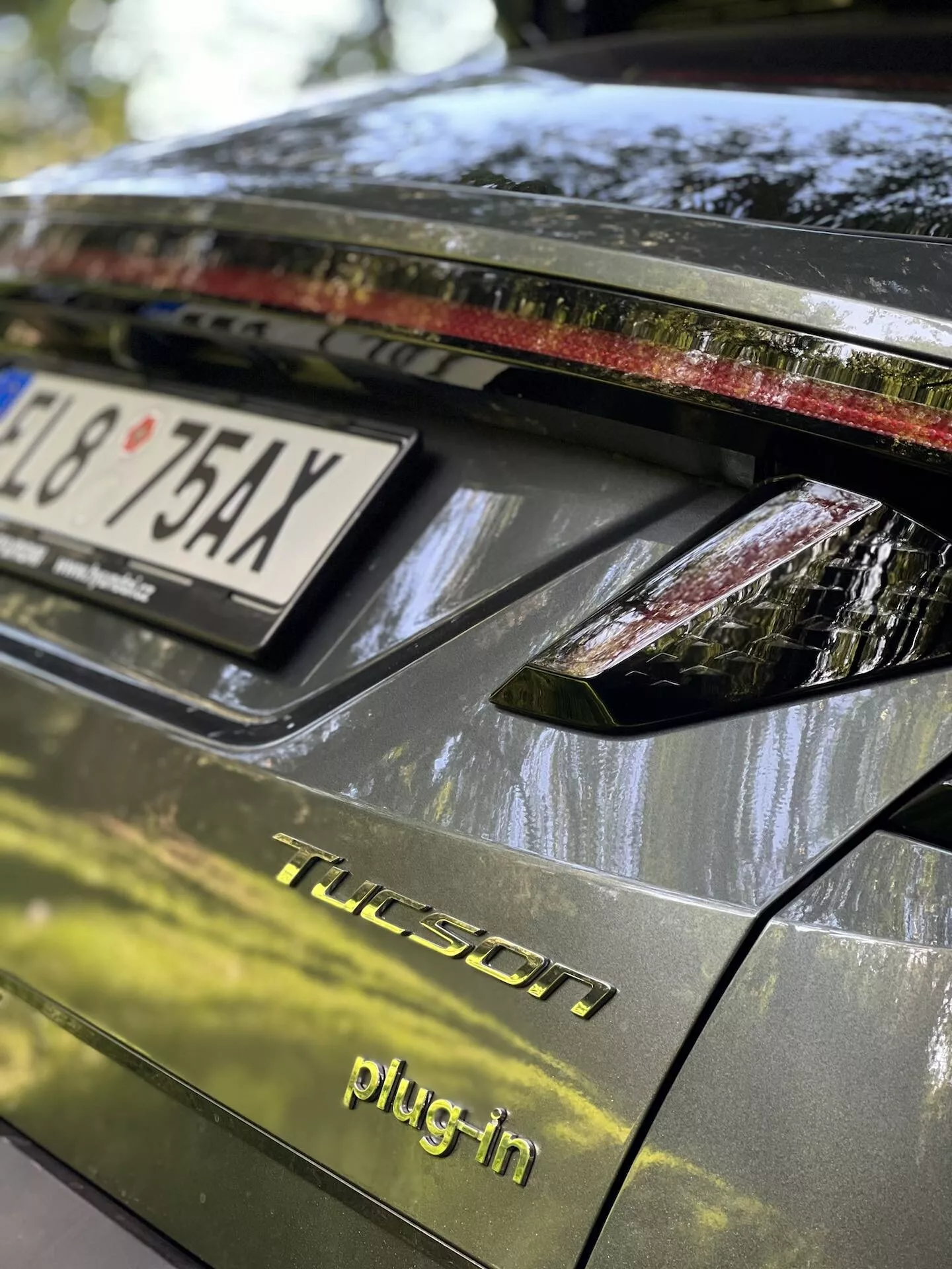 Zbliżenie na tylną część Hyundaia Tucson 2020 w wersji plug-in hybrid, przedstawiające pokrywę bagażnika, tylny zespół oświetleniowy z lampami LED, ciemne błyszczące wykończenie, i szczegóły wskazujące na parkowanie na zewnątrz