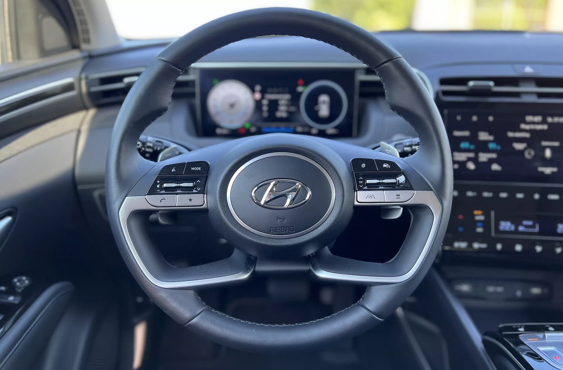 Widok wnętrza Hyundai Tucson 2020 z perspektywy miejsca kierowcy, pokazujący kierownicę z logo Hyundai, cyfrowy panel wskaźników i ekran systemu rozrywki