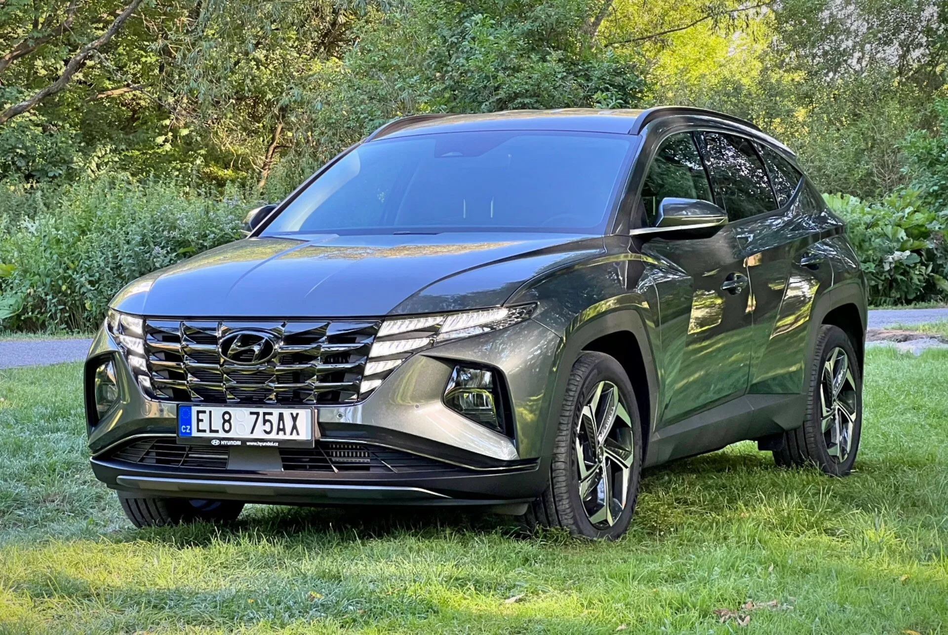 SUV Hyundai Tucson 2020 zaparkowany na trawie z drzewami w tle, pokazujący przedni grill, reflektory LED i felgi aluminiowe