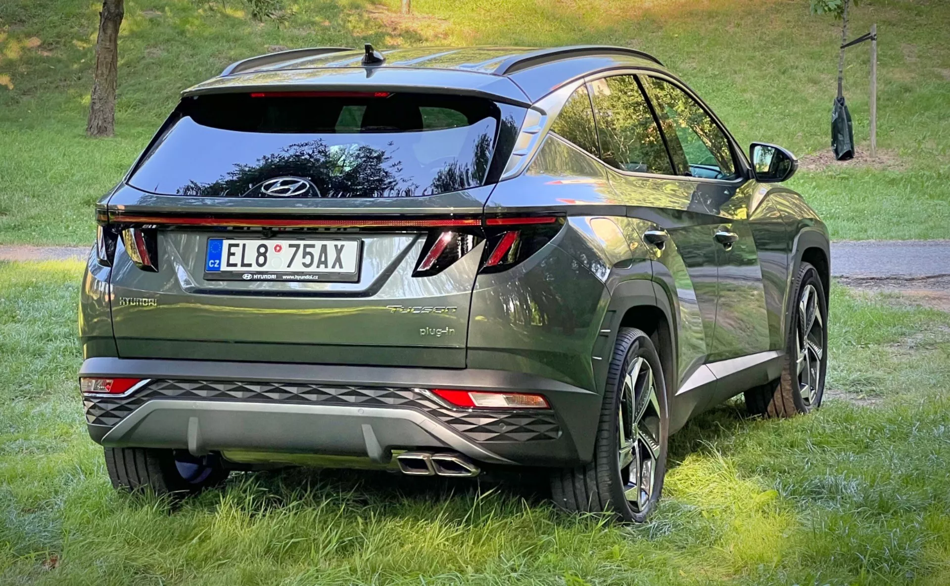 Trzy czwarte widoku z tyłu Hyundai Tucson 2020, prezentujące jego tylne światła LED, aerodynamiczną konstrukcję z spoilerem dachowym i anteną płetwy rekina, ekskluzywne wykończenie w ciemnozielonym metaliku, wyposażone w duże felgi aluminiowe i czujniki parkowania, w miejskim stylu crossover
