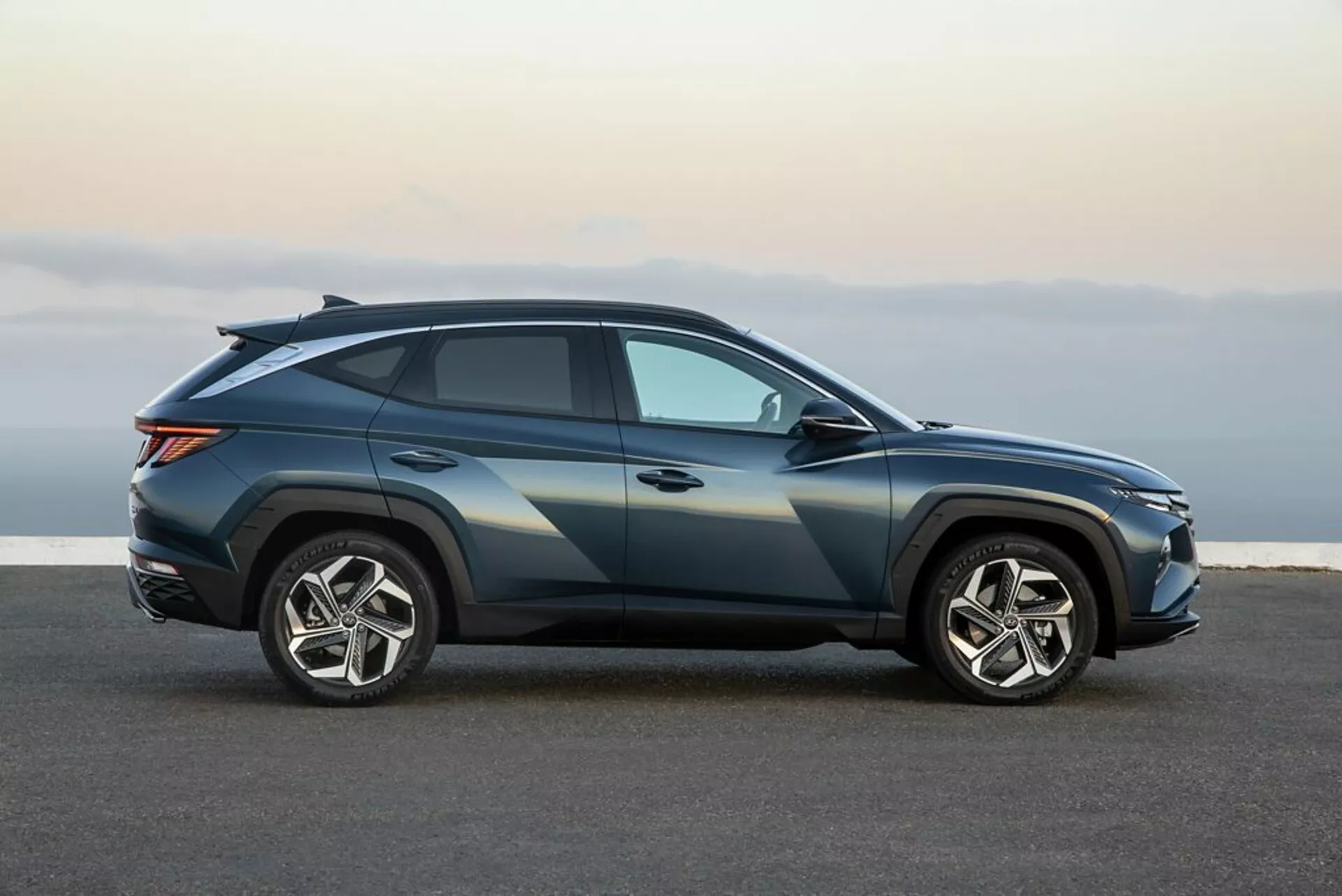 Zdjęcie profilowe Hyundai Tucson 2020 w ciemnoblue metallic z sportową linią dachu w stylu coupe, dużymi pięcioramiennymi kołami ze stopu i zaawansowanym oświetleniem, na asfaltowej nawierzchni wskazujące na elegancki design i cechy technologiczne