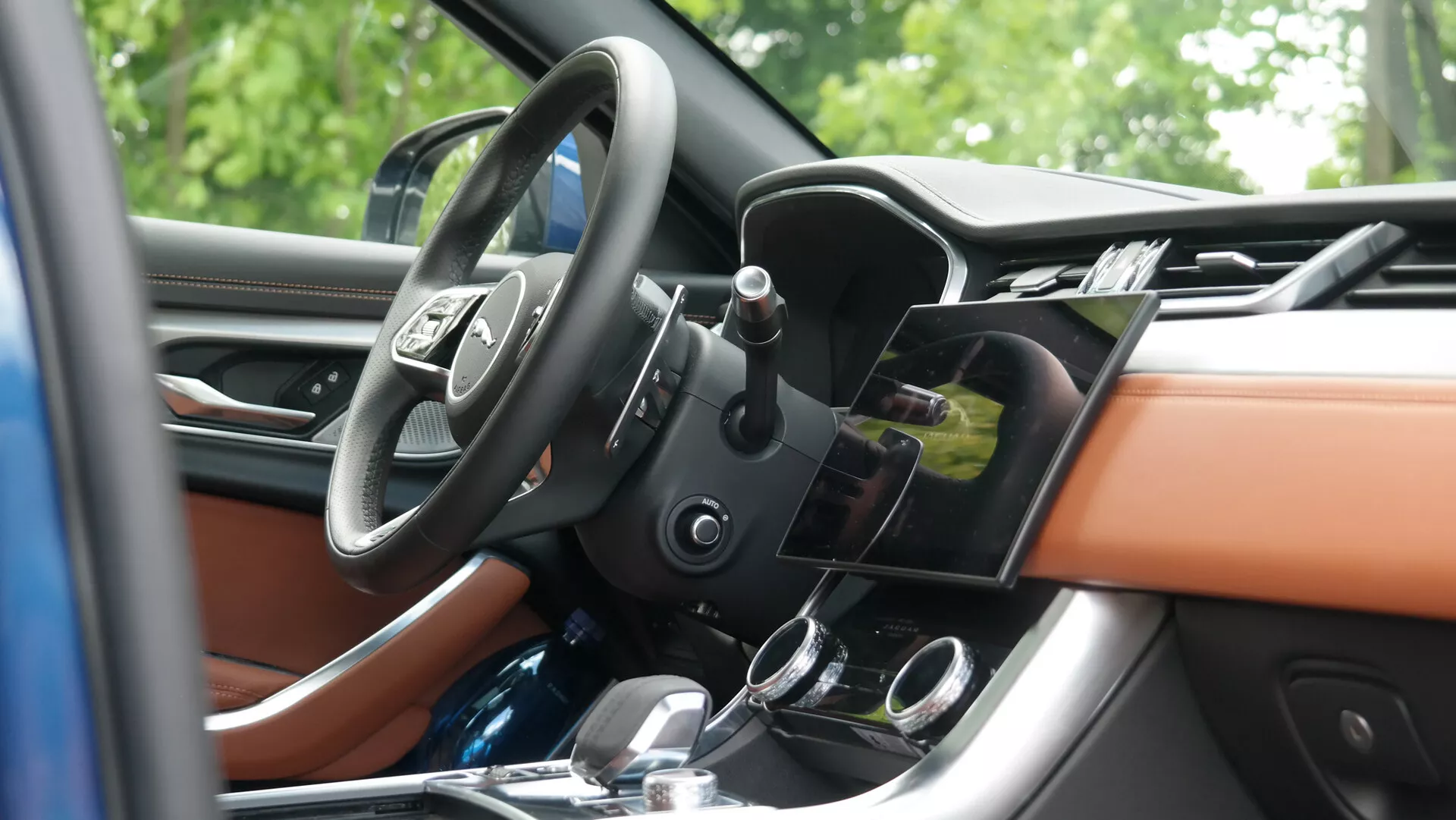 Luksusowe wnętrze Jaguara XF 2021 z jasnobeżową skórzaną tapicerką, deską rozdzielczą wykończoną drewnem, nowoczesnymi systemami informacyjno-rozrywkowymi i klimatyzacyjnymi oraz wielofunkcyjną kierownicą, widziane z zewnętrznego bocznego kąta.