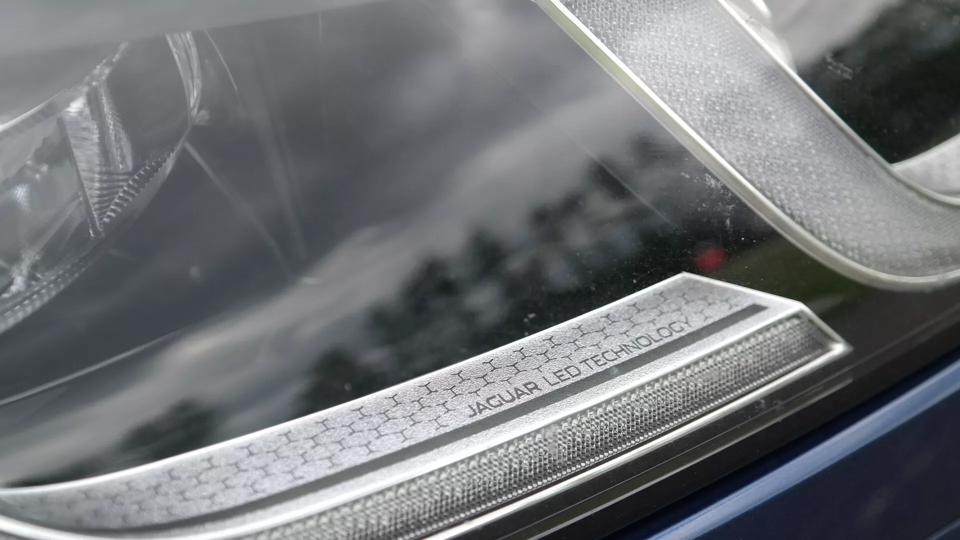 Zbliżenie na reflektor Jaguar XF 2021 z napisem 'Jaguar LED Technology', prezentujące zaawansowane oświetlenie LED, luksusowy design i szczegółowe rzemiosło z rozmytym tłem podkreślającym złożoną strukturę reflektora.