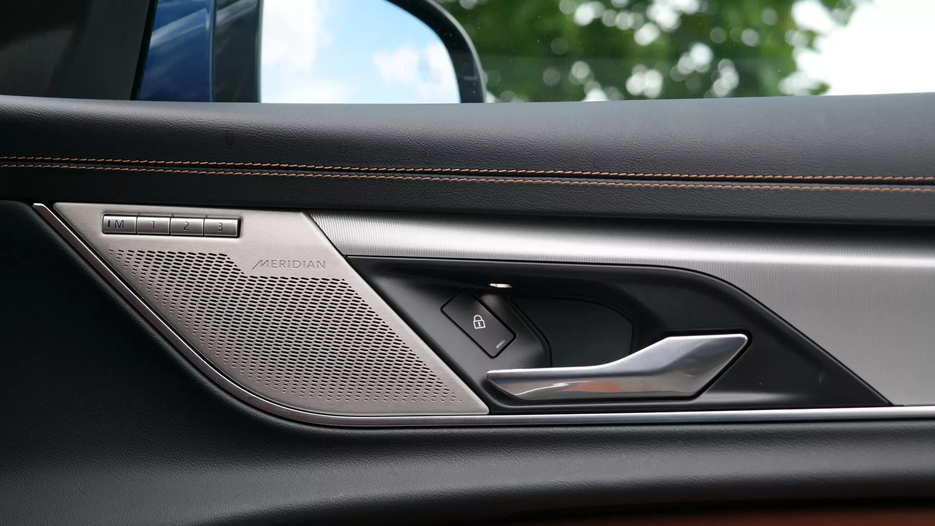 Zbliżenie na wewnętrzny panel drzwiowy Jaguara XF 2021, pokazujące wysokiej jakości głośnik systemu dźwiękowego Meridian, elegancką klamkę drzwi, przycisk centralnego zamka i luksusowo szyty, skórzany podłokietnik, podkreślające zaawansowaną technologię i wysokiej jakości materiały samochodu.