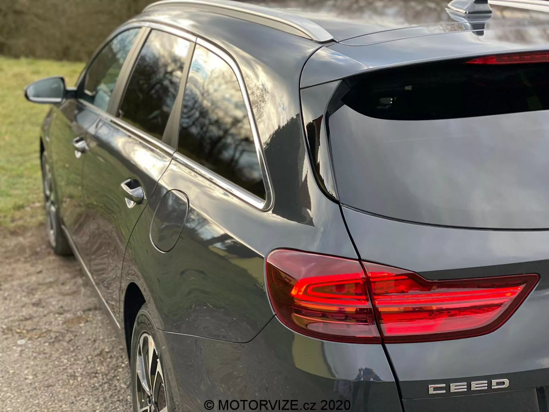 Częściowy widok boczny i tylny nowoczesnego szarego hatchbacka Kia Ceed 2018 z podkreślonym podświetlonym tylnym światłem LED w kształcie litery C, konstrukcją hatchbacka z tylną wycieraczką i subtelnym spojlerem dachowym, anteną w kształcie płetwy rekina, felgami z stopu i odznaką marki z nazwą modelu 'CEED', uchwyconym w naturalnym późnopopołudniowym świetle i małą głębią ostrości skupiającą się na pojeździe.