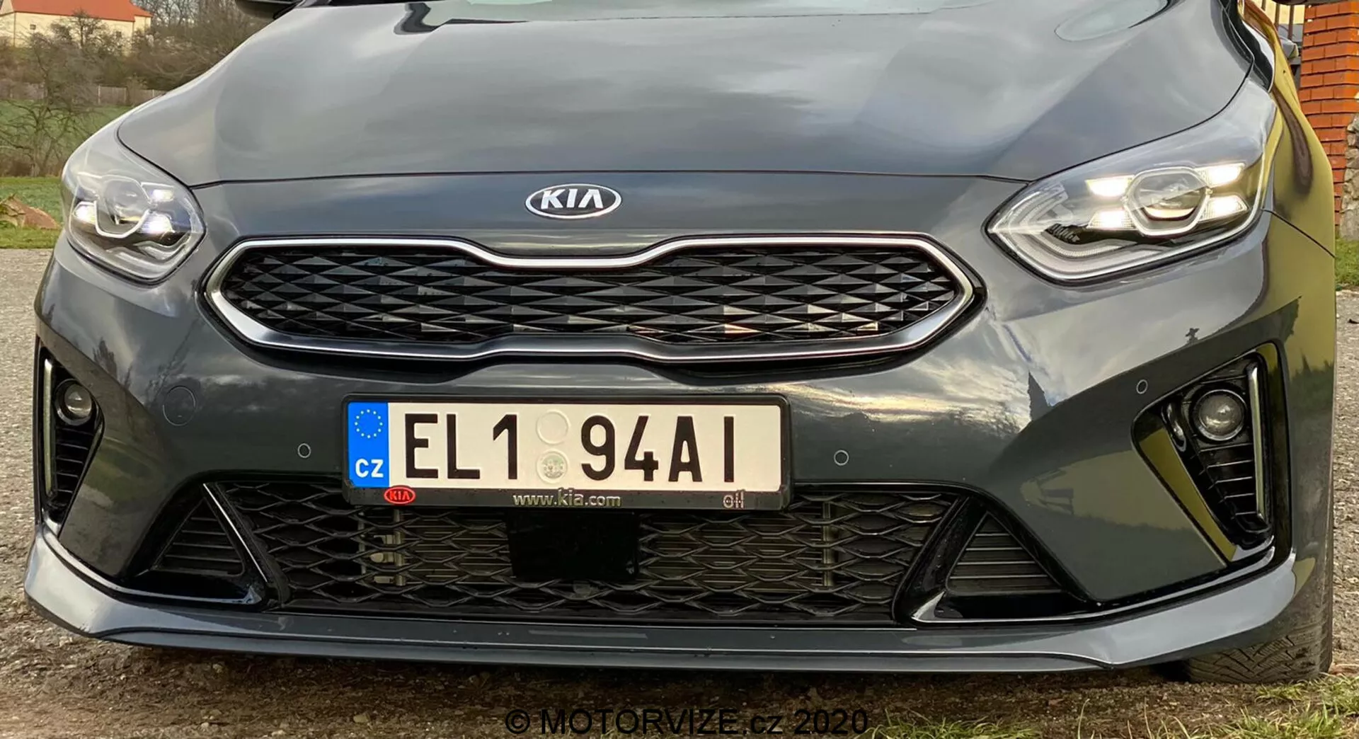 To zdjęcie przedstawia przedni koniec pojazdu Kia Ceed 2018 zrobione pod niskim kątem. Podkreśla eleganckie, poziome reflektory LED, wyraźną kratkę z wzorem plastra miodu z centralnym emblematem Kia, europejską tablicę rejestracyjną z Czech oraz sportowy przedni zderzak z dużymi otworami. Zbliżenie uwydatnia czujniki parkowania pod kratką. Sportowy design sugeruje wyższą wersję wyposażenia, choć dokładne specyfikacje nie są jasne. Obraz w wysokiej rozdzielczości uchwyca szczegóły projektowe i kontury pojazdu, z lekko przesuniętym kątem w lewo.