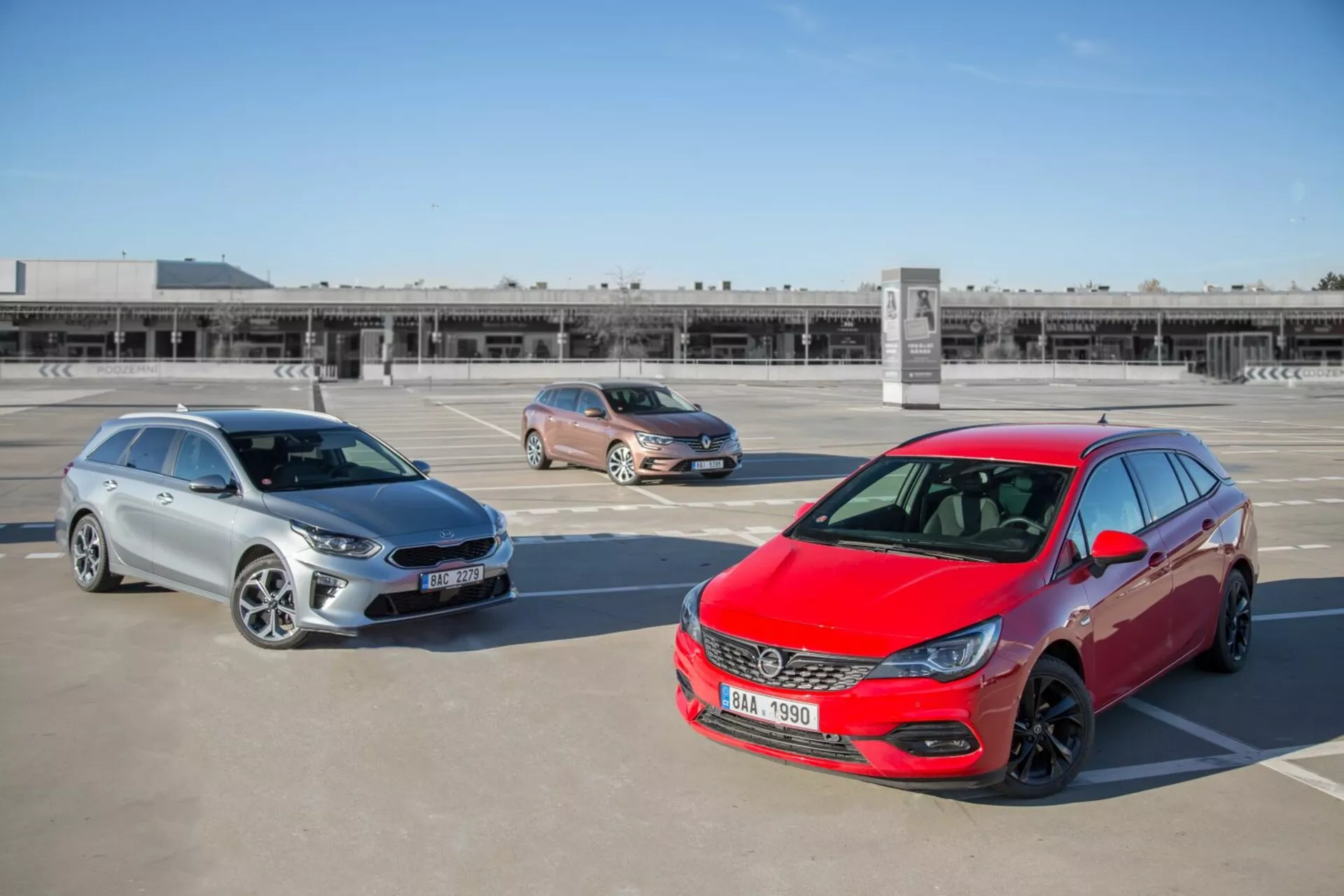 Trzy modele Kia Ceed z 2009 roku, w tym czerwony hatchback, złoty crossover i srebrne kombi zaparkowane na dachu parkingu, sfotografowane z wyższej pozycji ukazującej design przedniej części, profile boczne i długość pojazdów