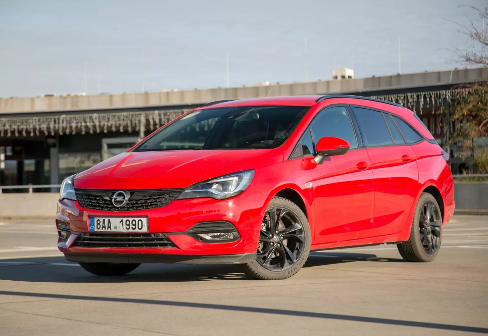 Jaskrawoczerwony hatchback Kia Ceed z 2009 roku zaparkowany na gładkim betonie pod jasnym niebem, prezentujący LEDowe reflektory, elegancką kratę, ciemne felgi aluminiowe i nowoczesny design aerodynamiczny z perspektywy trzech czwartych z przodu w ciągu dnia.