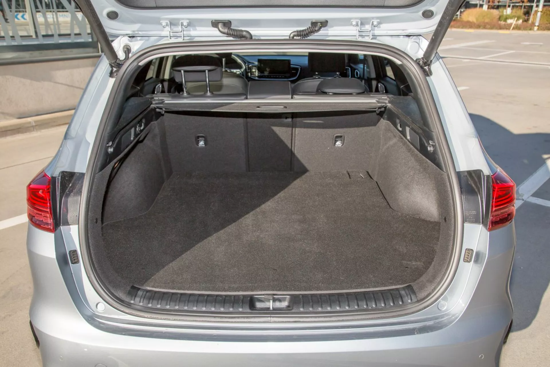 Tylny przedział bagażowy hatchbacka Kia Cee'd 2009 z otwartą klapą, prezentujący przestronną czystą przestrzeń bagażową, wykładzinę, chowaną osłonę i potencjalne oświetlenie wnętrza