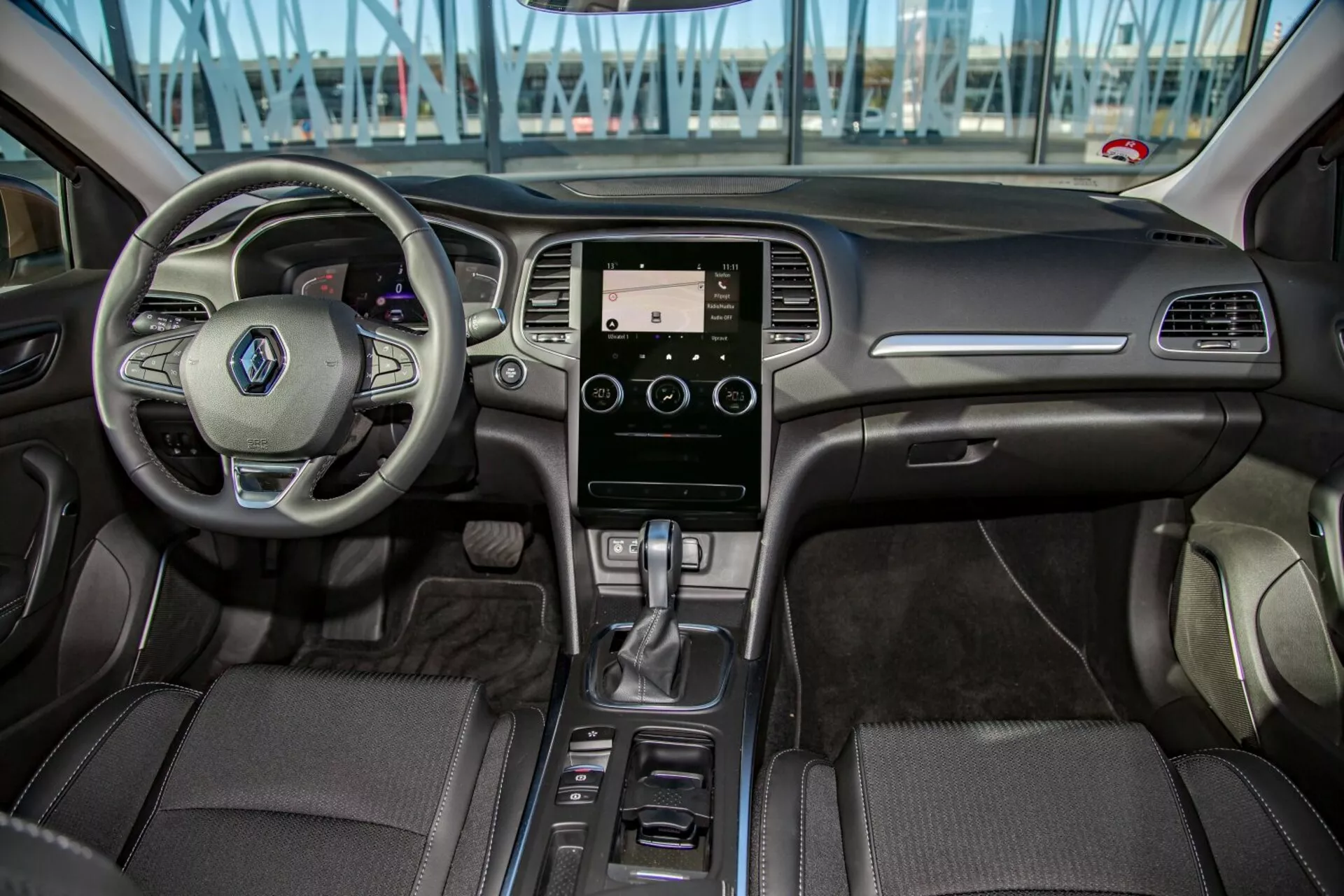 Wnętrze Kia Cee'd 2009 widziane z tylnego siedzenia, pokazujące wielofunkcyjną kierownicę, system infotainmentu dotykowego, automatyczną dźwignię zmiany biegów i szczegółową tapicerkę w przedniej części kokpitu